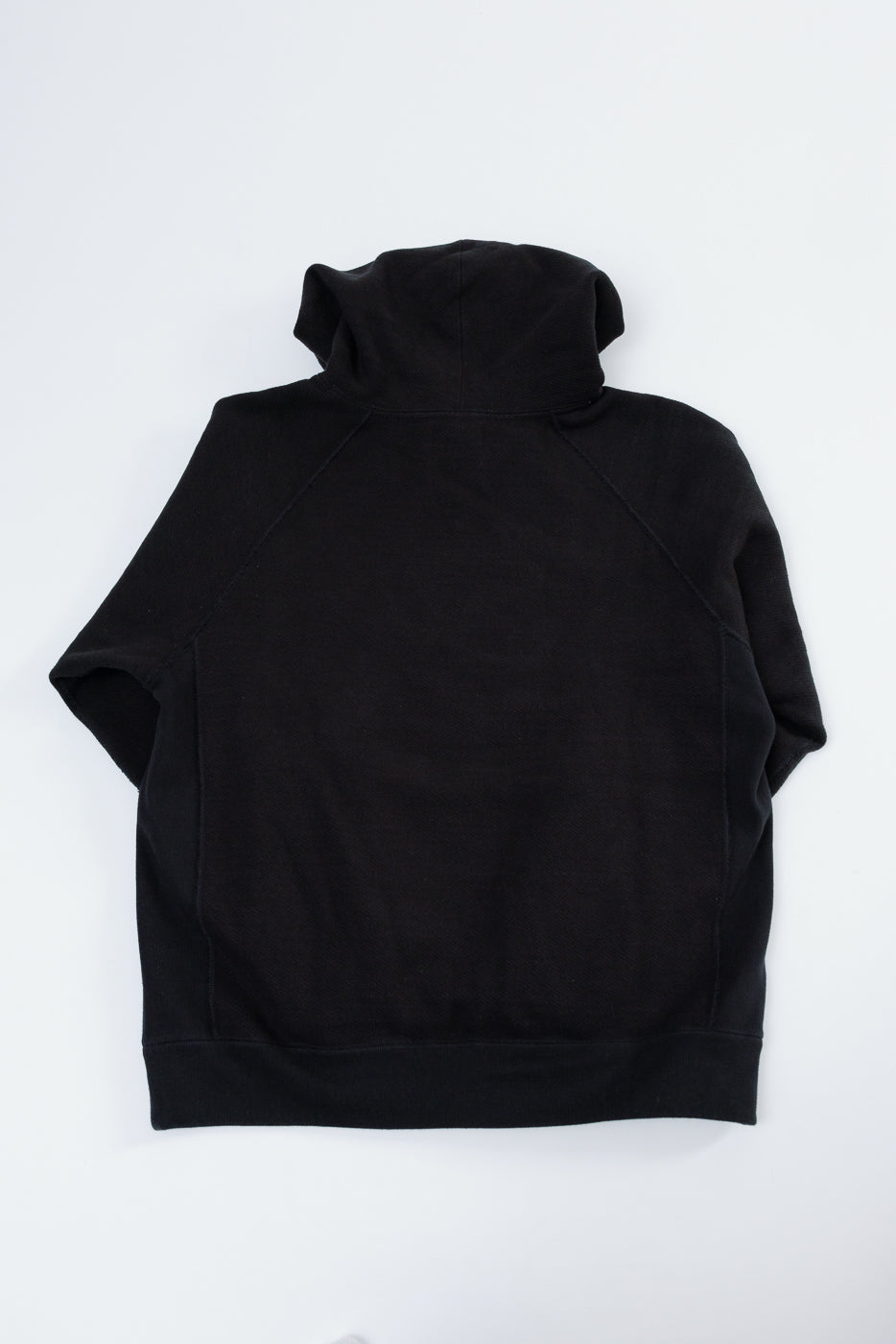 Back view flat lay of a black hooded sweatshirt showing the hood and raglan sleeve construction.