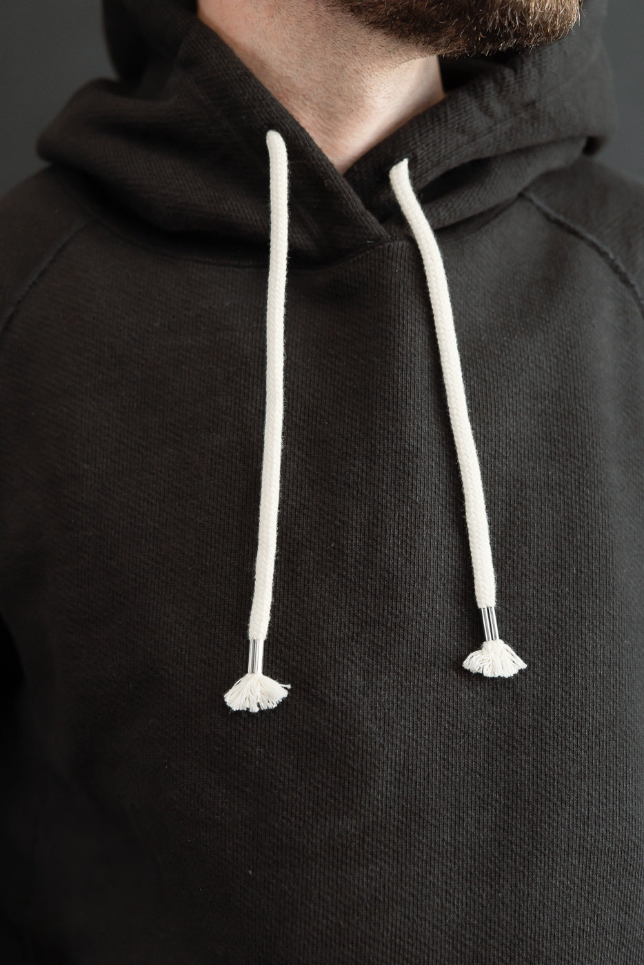 Close-up front view of a black hoodie with white drawstrings on a 5'9