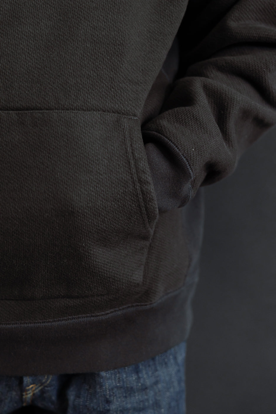 Close-up of the right side and front pocket of a dark brown textured hoodie on a male model.