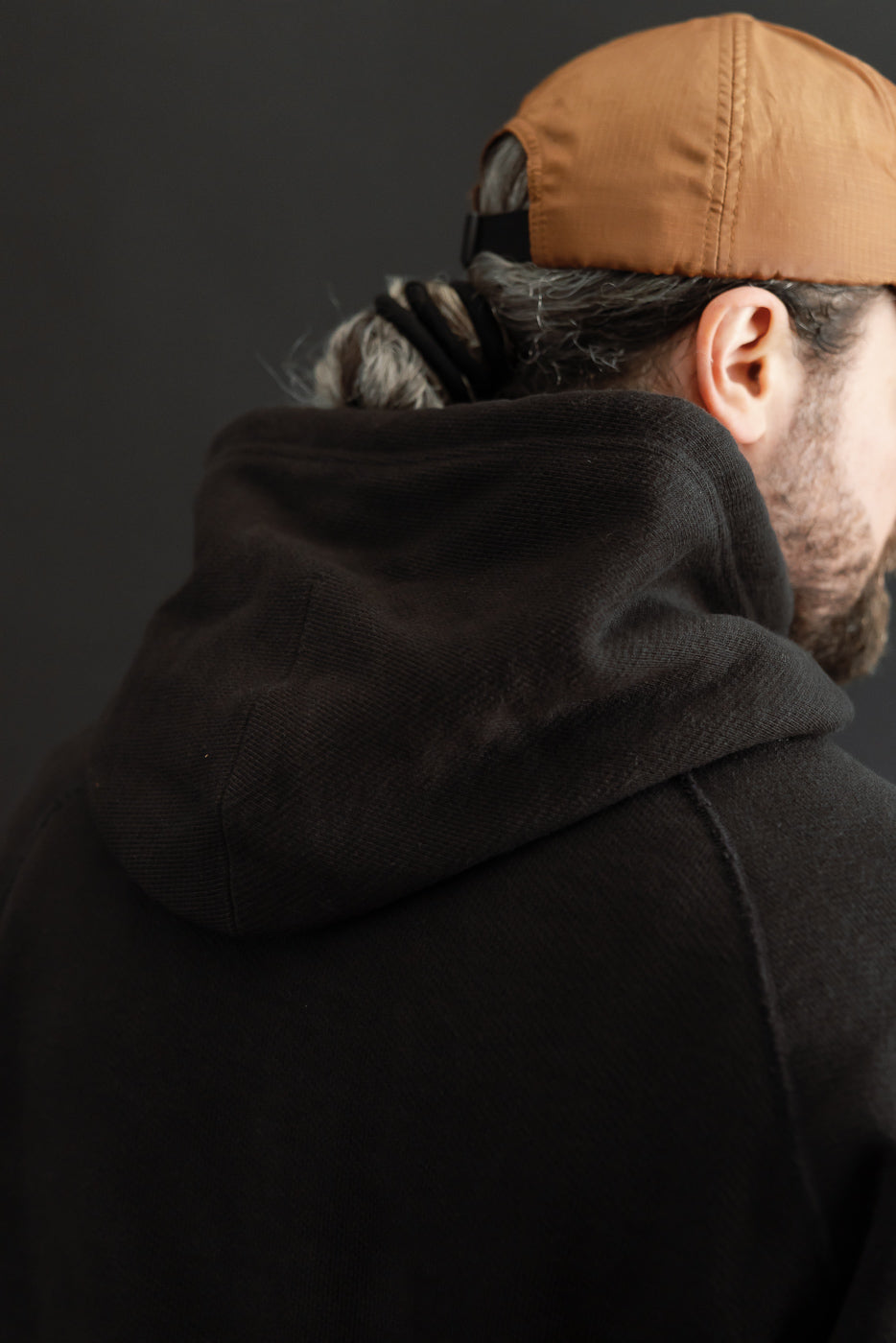 Close-up back view of a black hooded sweatshirt on a male model, showing the hood texture.