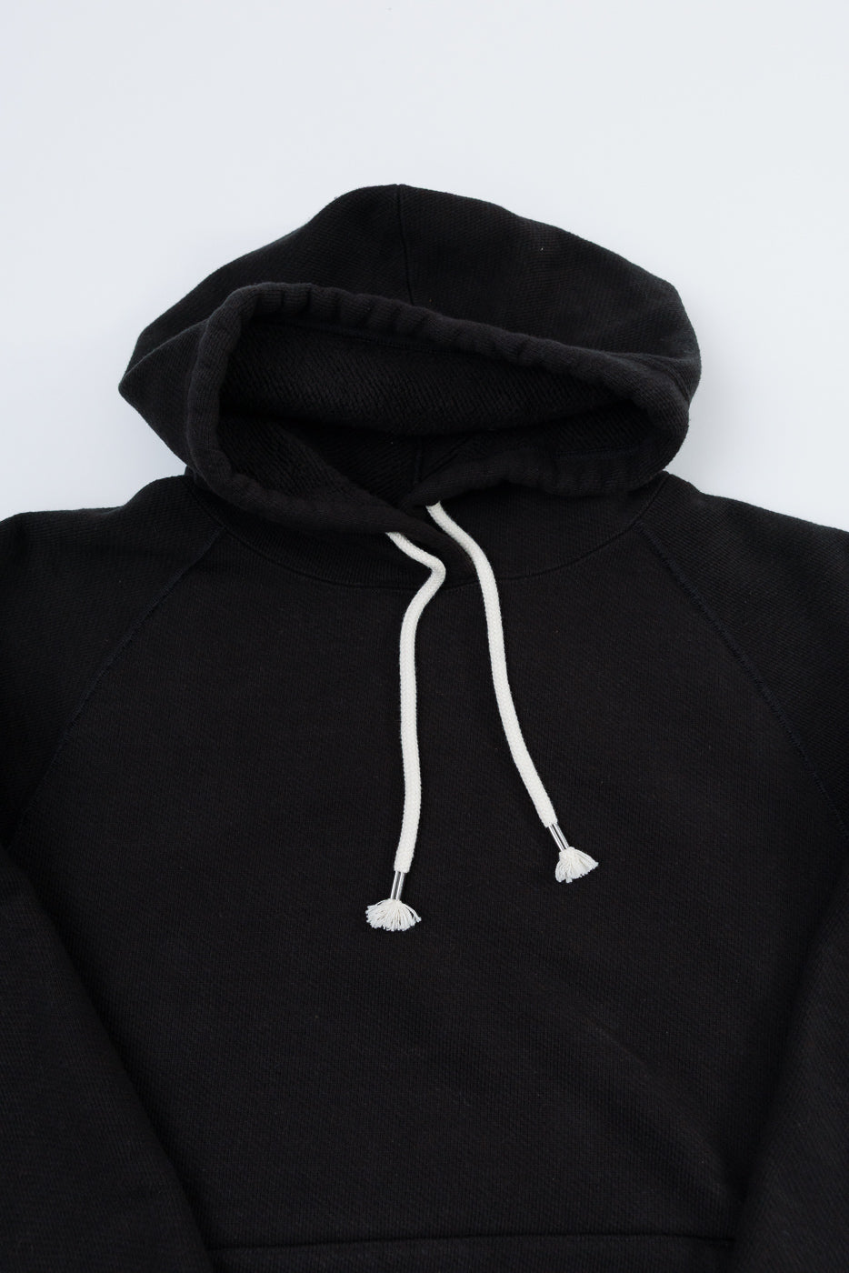 Front view flat lay of a black hoodie featuring white drawstrings and a ribbed hood.