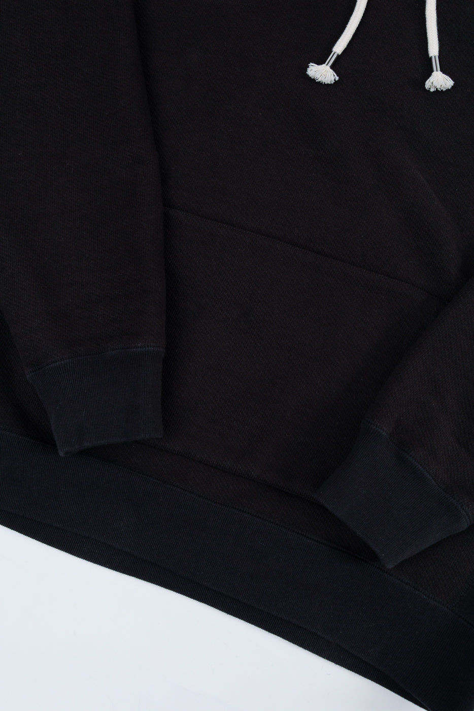 Close-up front view of a black hoodie showing the drawstring, kangaroo pocket, and ribbed cuffs.