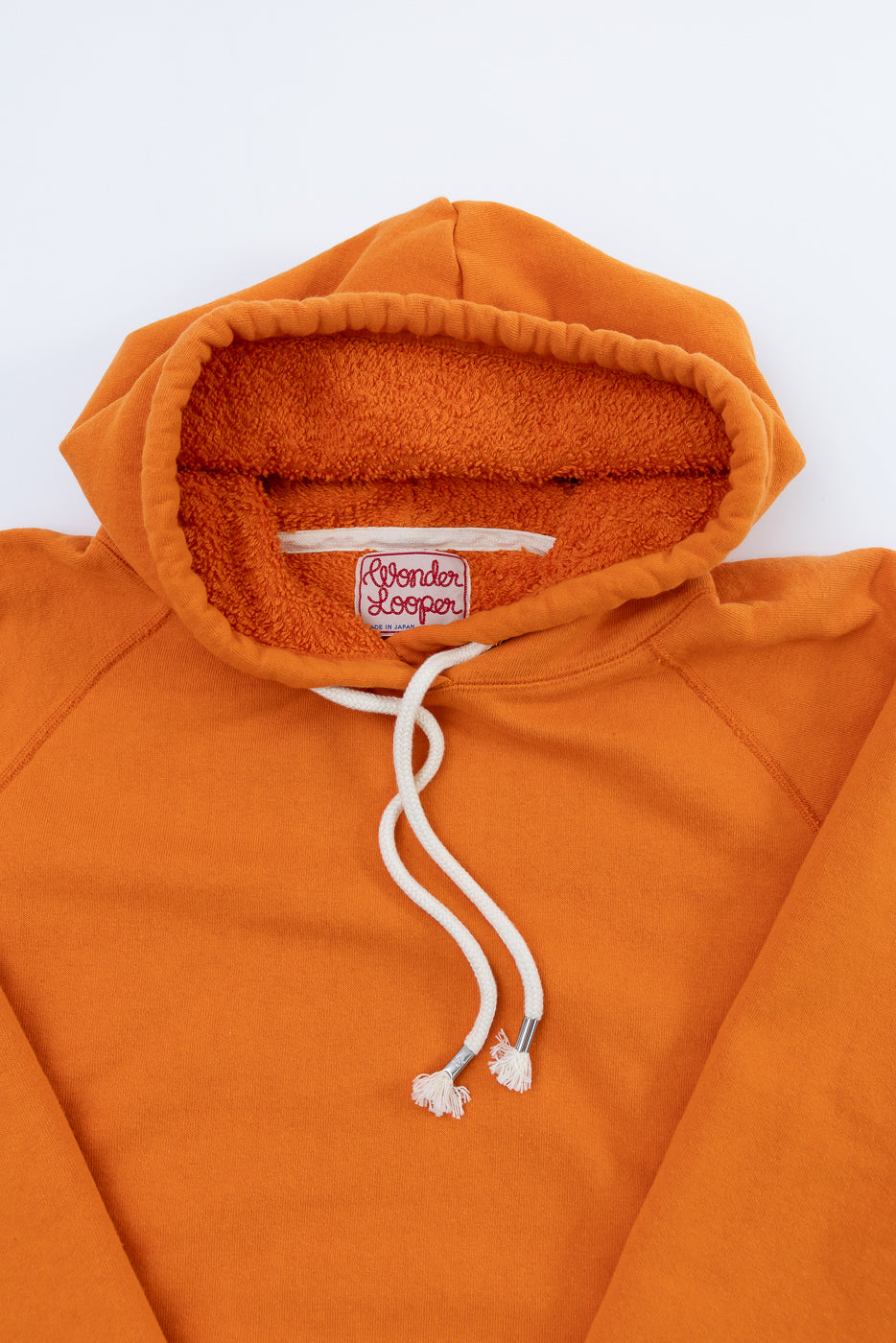 Pullover Hoodie - Super Looper French Terry - Orange, featuring a terry-cloth lined hood with white drawcords and metal aglets, woven Wonder Looper label inside the collar, laid flat against a white background.