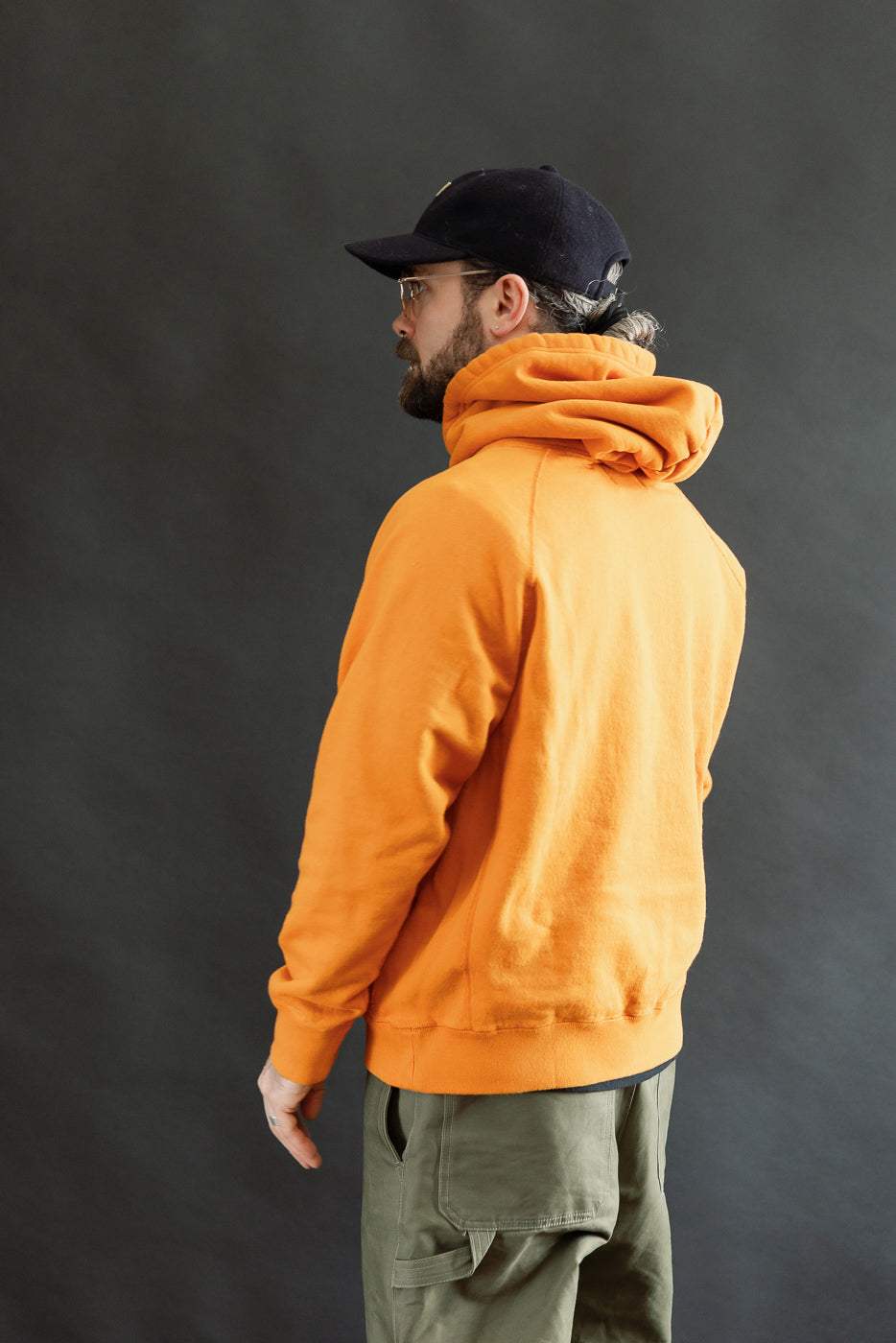 Man in profile wearing the Pullover Hoodie - Super Looper French Terry - Orange, showcasing its smooth exterior and modern athletic fit, with visible raglan sleeves and a drawstring hood.