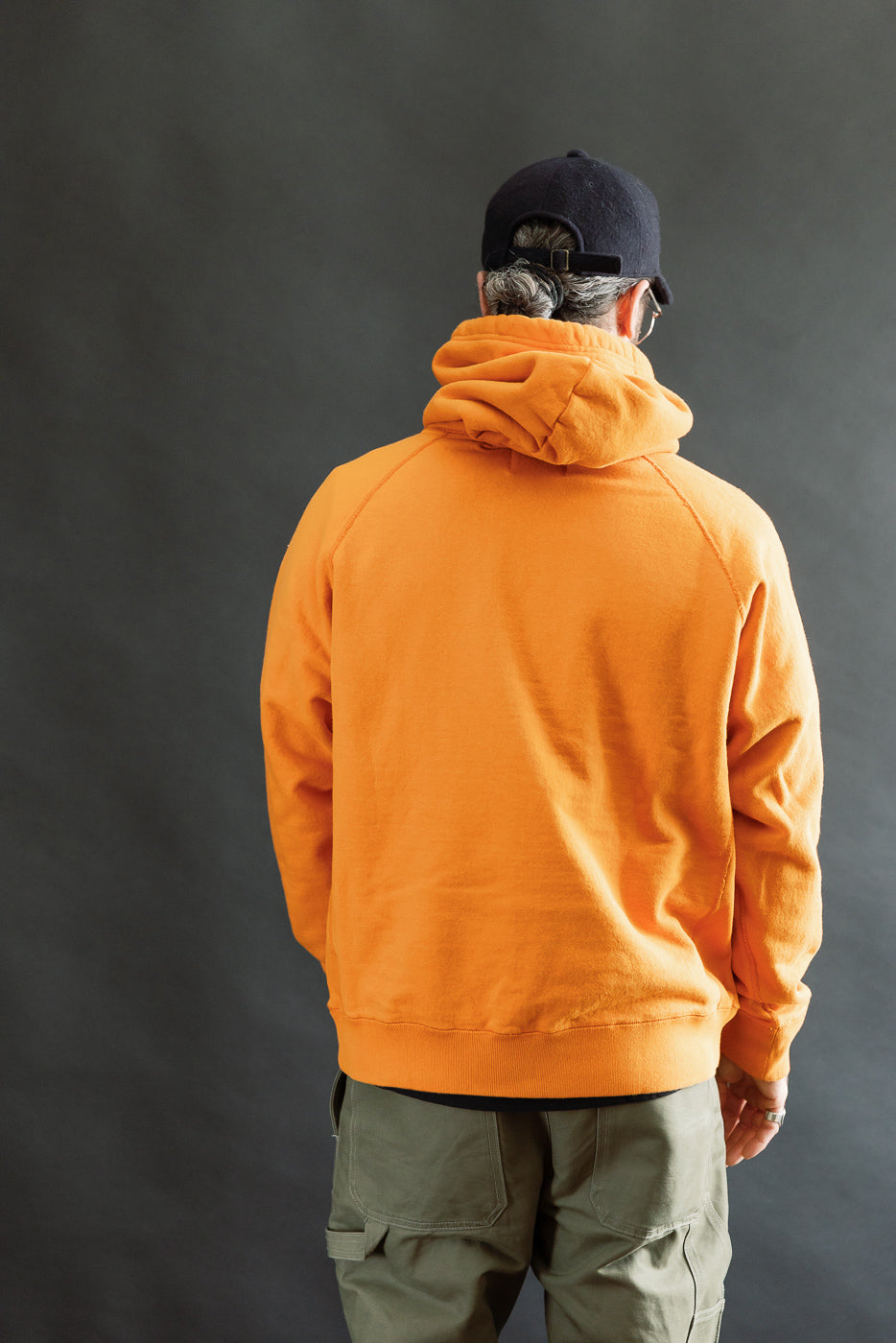 Person wearing the Pullover Hoodie - Super Looper French Terry - Orange, showcasing its modern athletic silhouette and smooth exterior. The hoodie features raglan sleeves, a drawstring hood, and a kangaroo pocket.