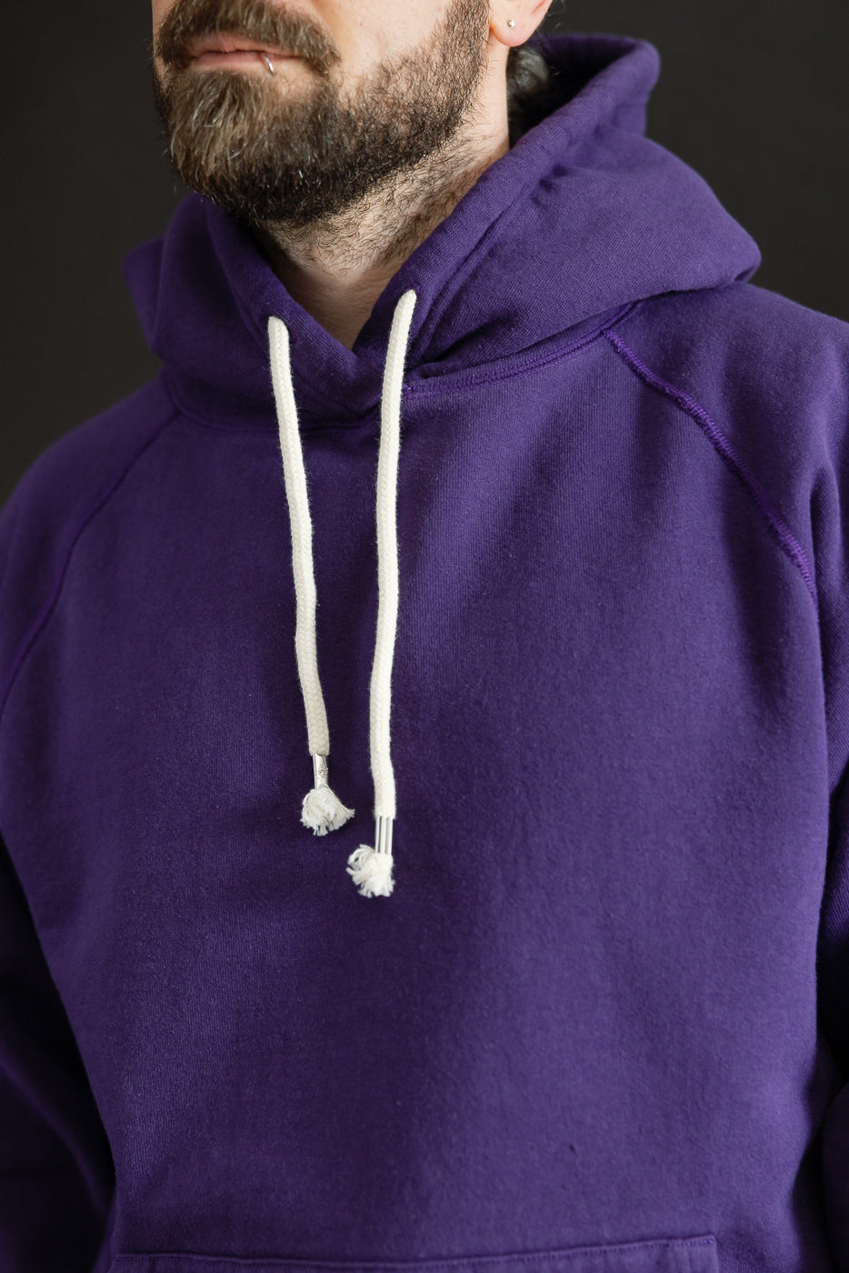 Close-up of a person wearing the Pullover Hoodie - Super Looper French Terry - Purple, showcasing its smooth exterior, white drawstrings, and distinctive athletic-fit silhouette. The hoodie exemplifies premium Japanese craftsmanship.
