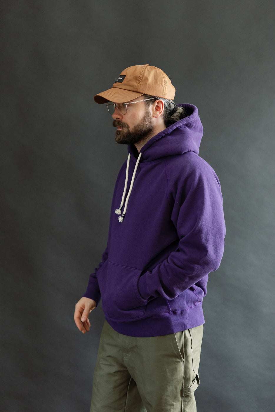 Bearded man in profile wearing the Pullover Hoodie - Super Looper French Terry - Purple, showcasing its smooth exterior and classic kangaroo pocket, embodying Dant's premium Japanese fabric focus.