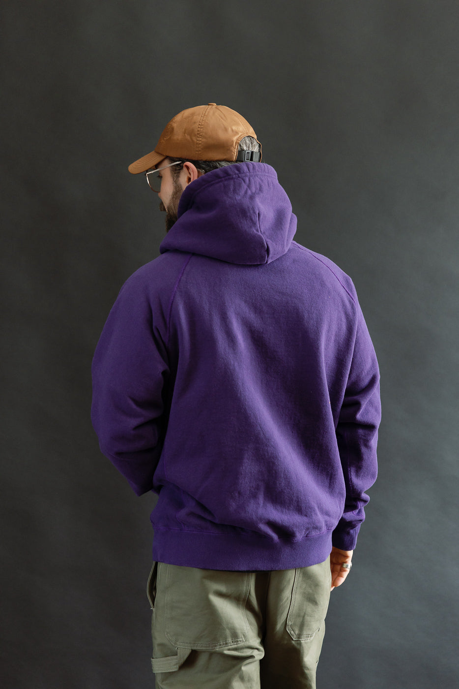 Man wearing the Pullover Hoodie - Super Looper French Terry - Purple, showcasing its athletic fit and smooth exterior, with relaxed arms, styled for a casual outdoor look.