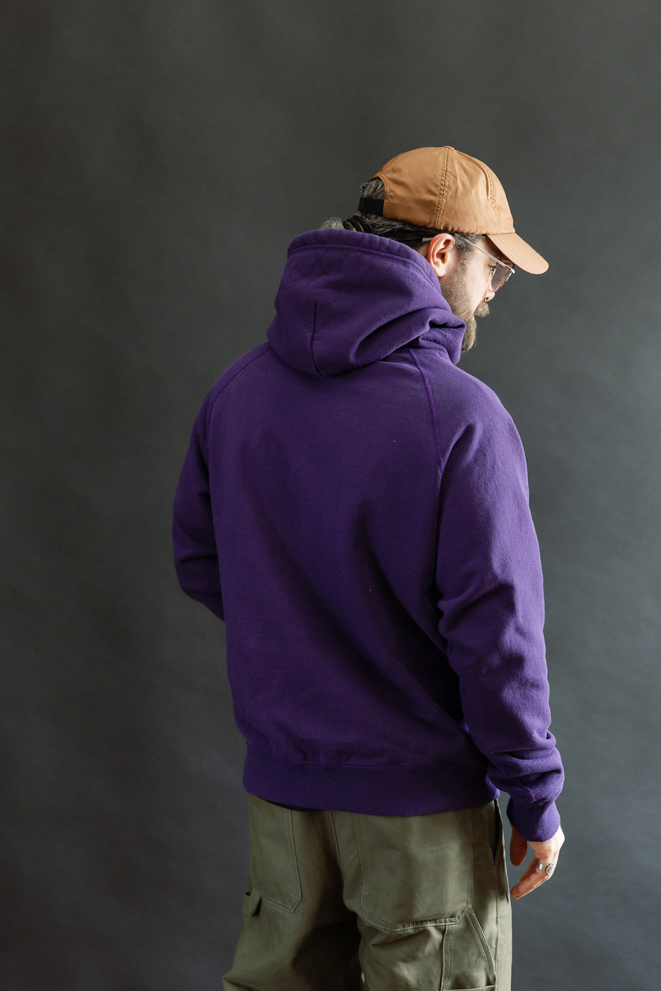 Man showcasing the Pullover Hoodie - Super Looper French Terry - Purple, styled with olive cargo pants and tan cap. Features include smooth exterior and plush interior crafted from Japanese Tsuriami knit fabric.