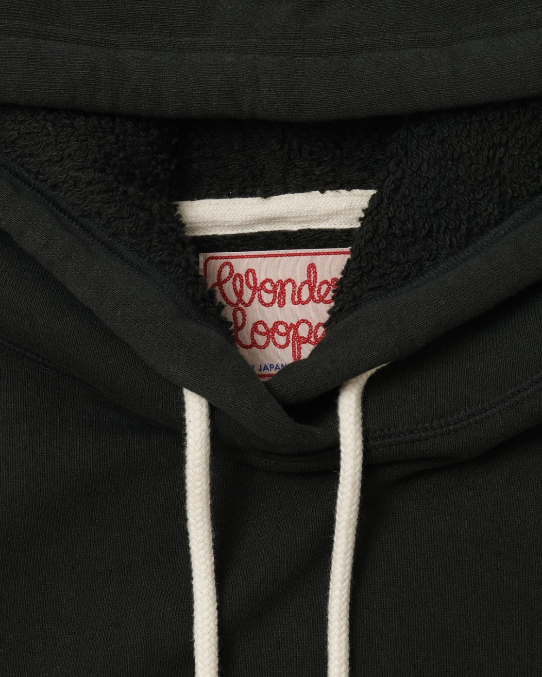 Close-up of front hoodie neckline showing drawstrings, textured French terry fabric, and interior tag.