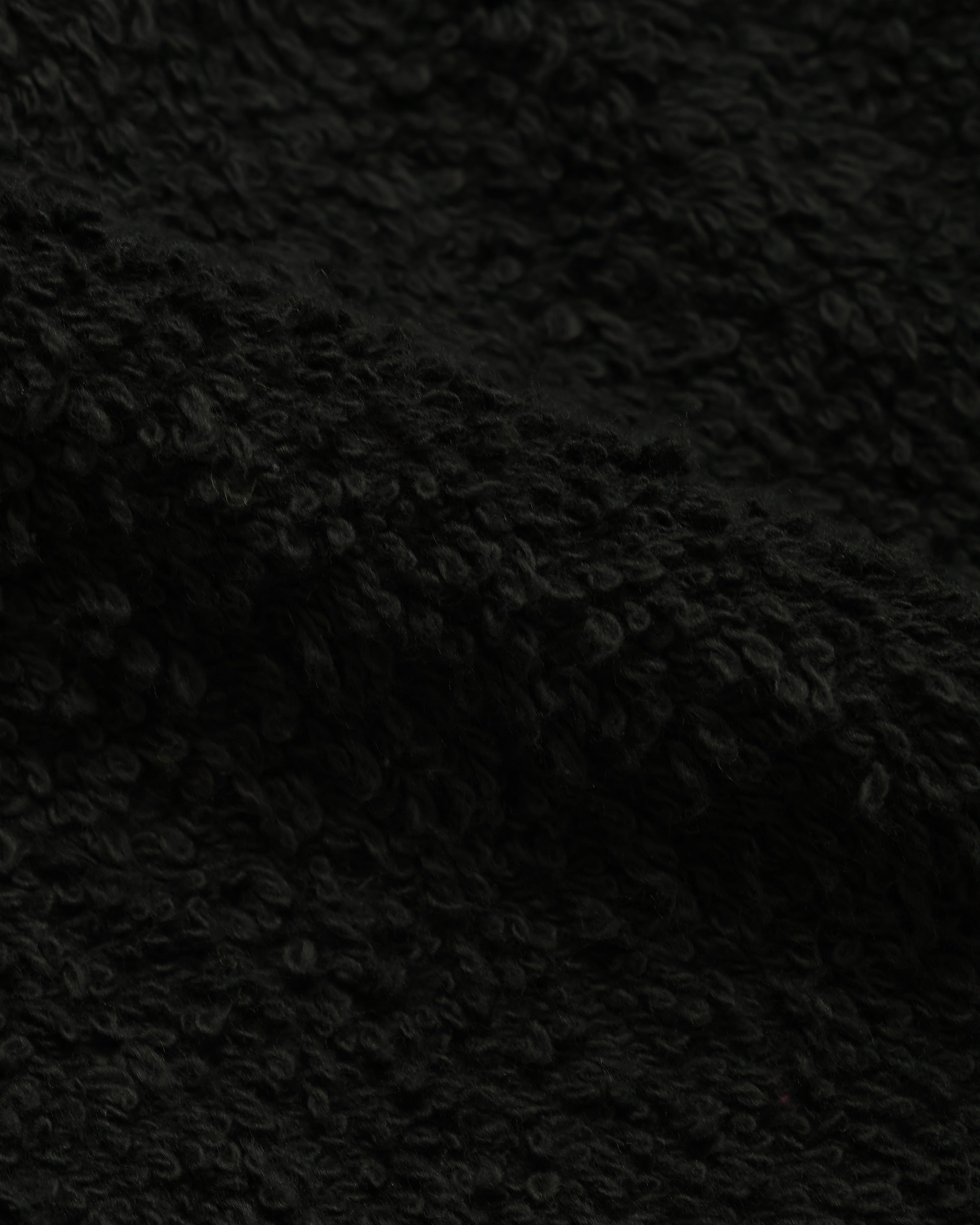 Close-up of black French terry pullover hoodie fabric, highlighting looped texture.