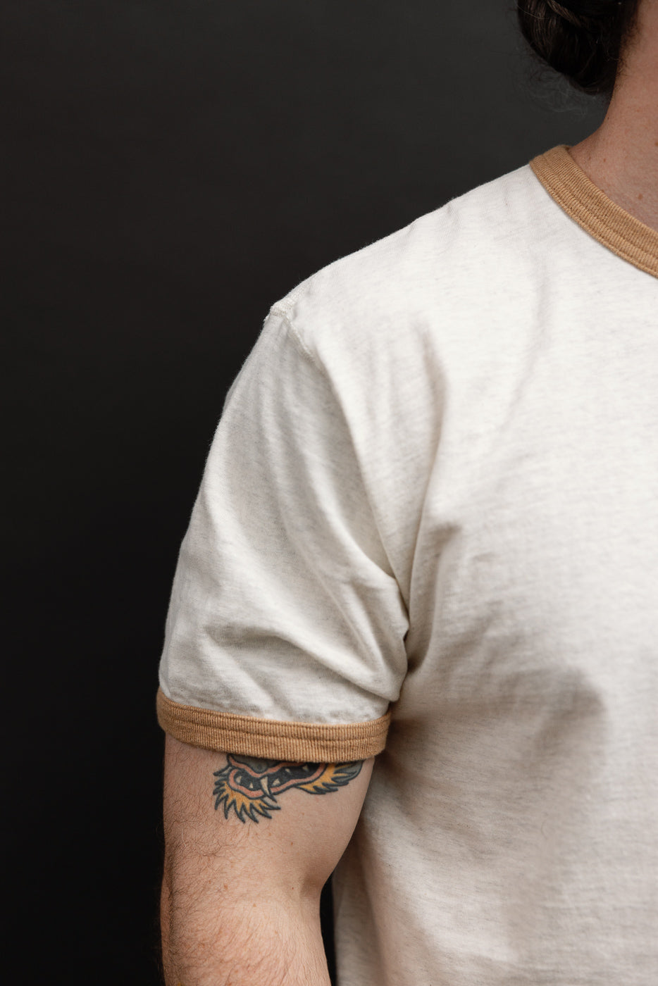 Close-up side view of a white ringer t-shirt with tan ribbed sleeve hem on a male model.