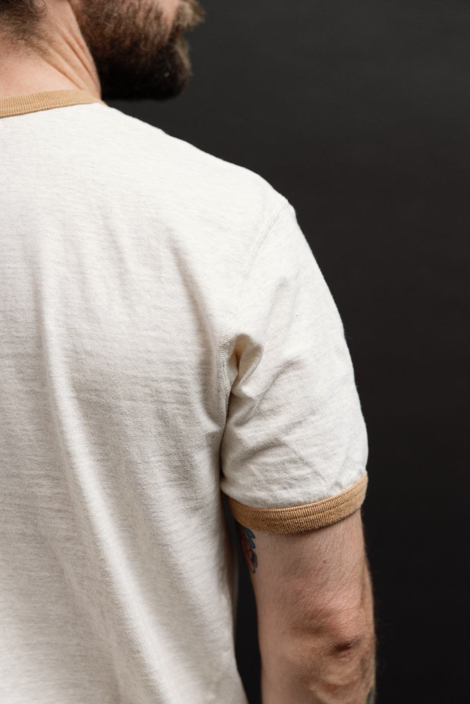 Close-up side view of a male model's white ringer t-shirt showing the tan ribbed sleeve hem.
