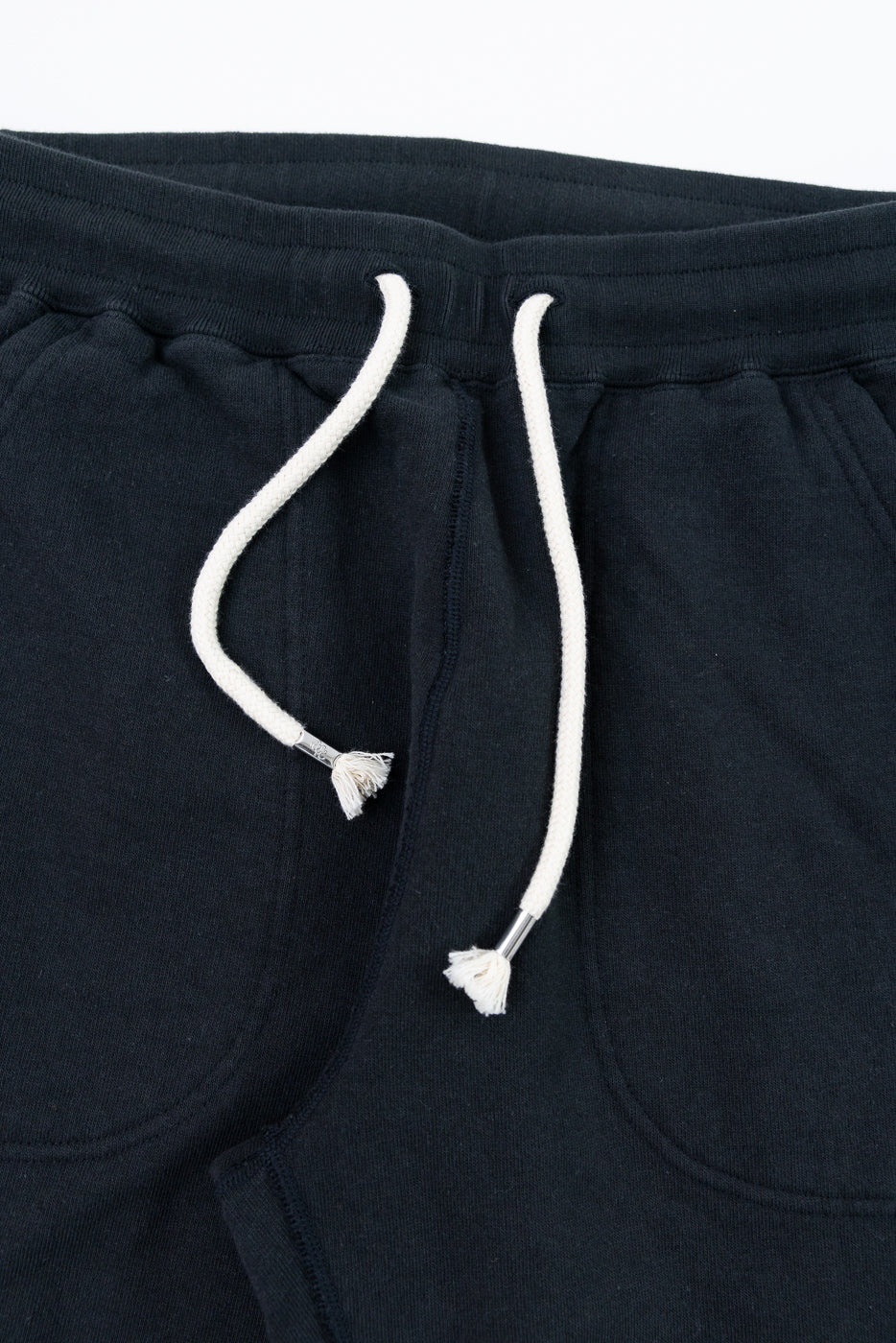 Close-up front of black joggers with white drawstrings and tassels, showing waistband and pocket details