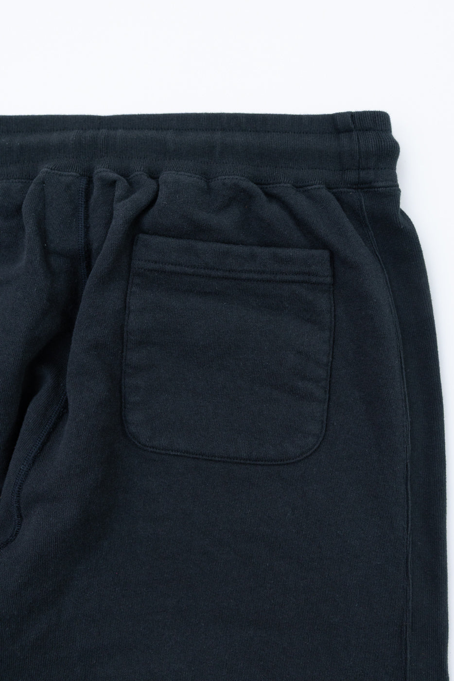 Close-up back view of black sweatpants showing rear pocket, ribbed waistband, and drawstring details