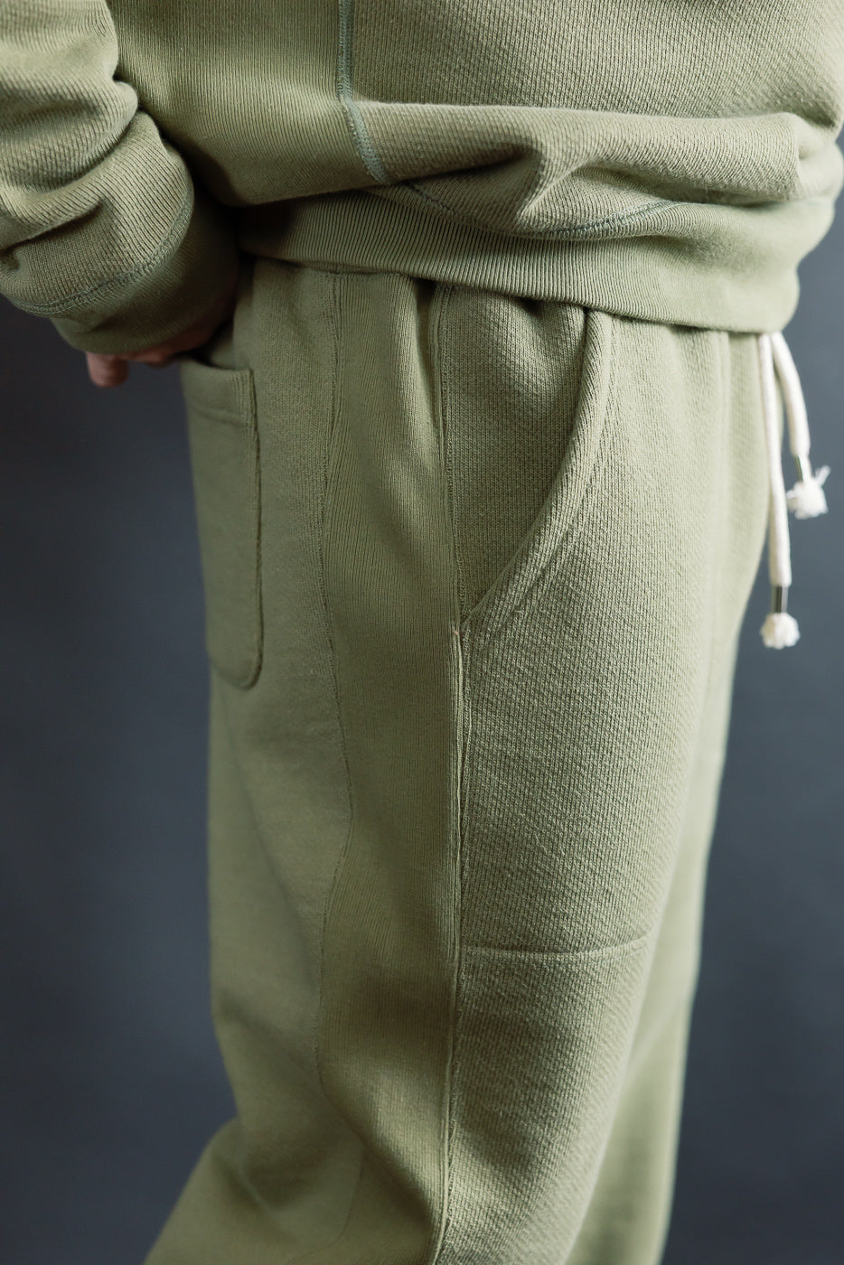 Close-up side view of sage French terry sweatpant pocket on male model, 5'9