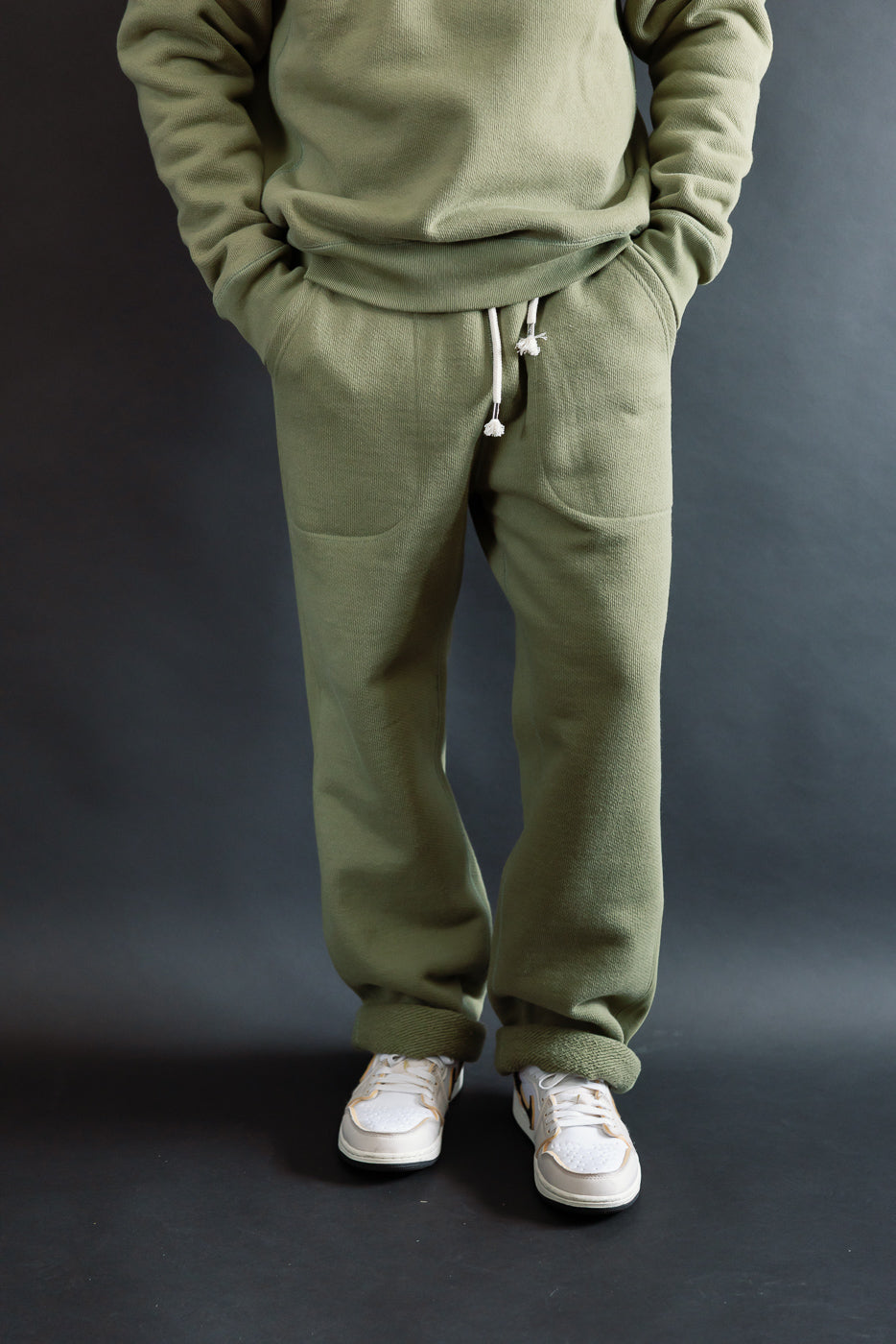 Front view of sage green double heavyweight French terry sweatpants on 5'9 male model, athletic build, hands in pockets, showing drawstring waist and full pant length.