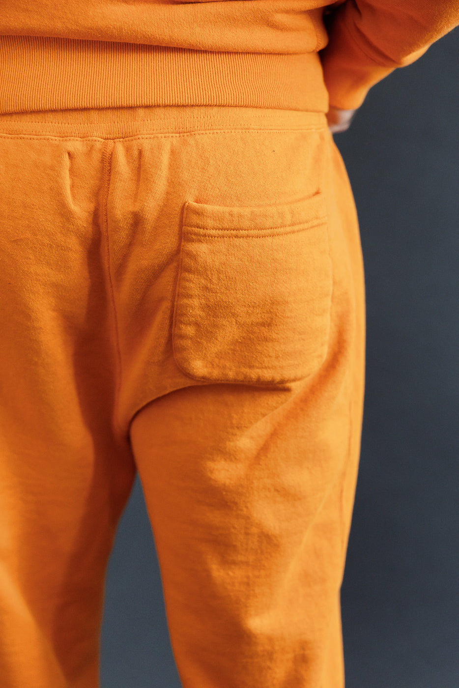 Close-up of male model's back showing orange sweatpants with rear pocket, athletic build