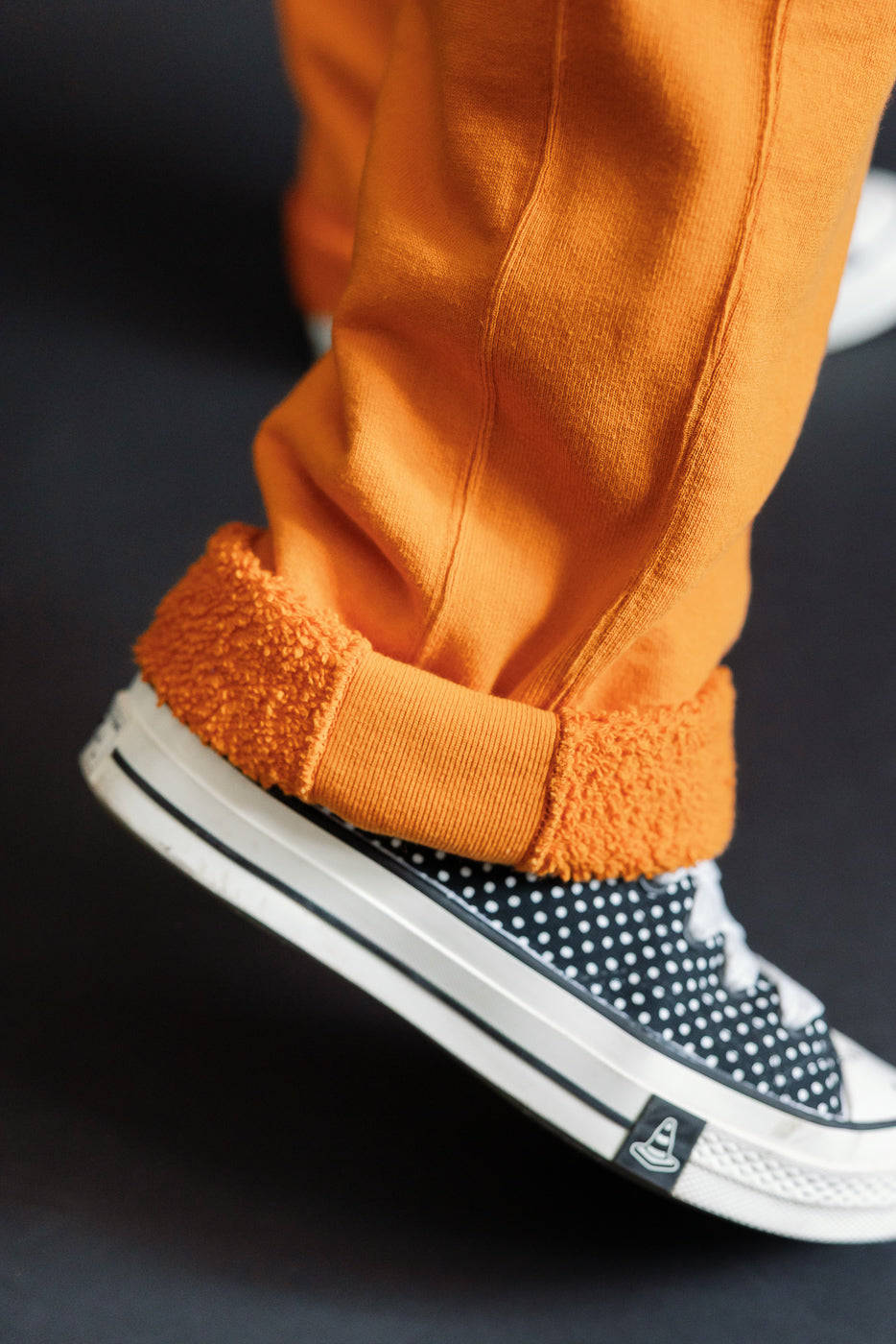 Close-up of male model's lower legs in orange fleece-lined pants, paired with polka-dot sneakers.