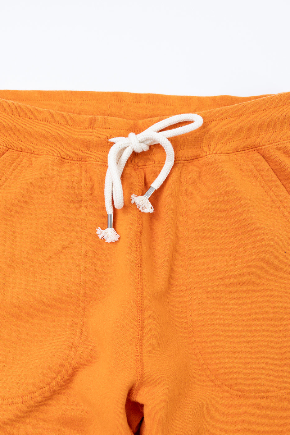 Close-up front view of orange sweatpants with white drawstring, metal aglets, and front pockets