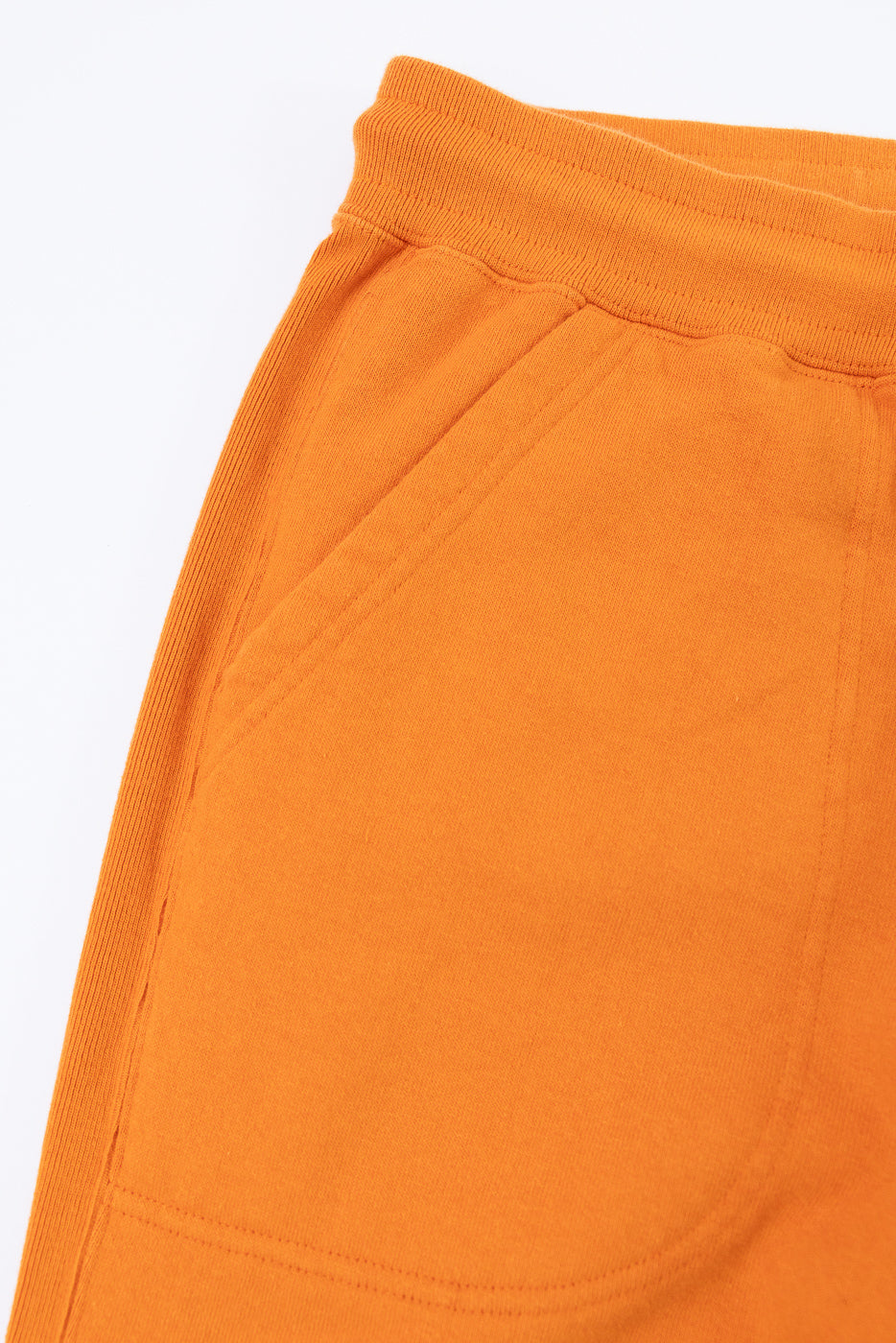 Close-up of orange sweatpants front, showing ribbed waistband and side pocket detail
