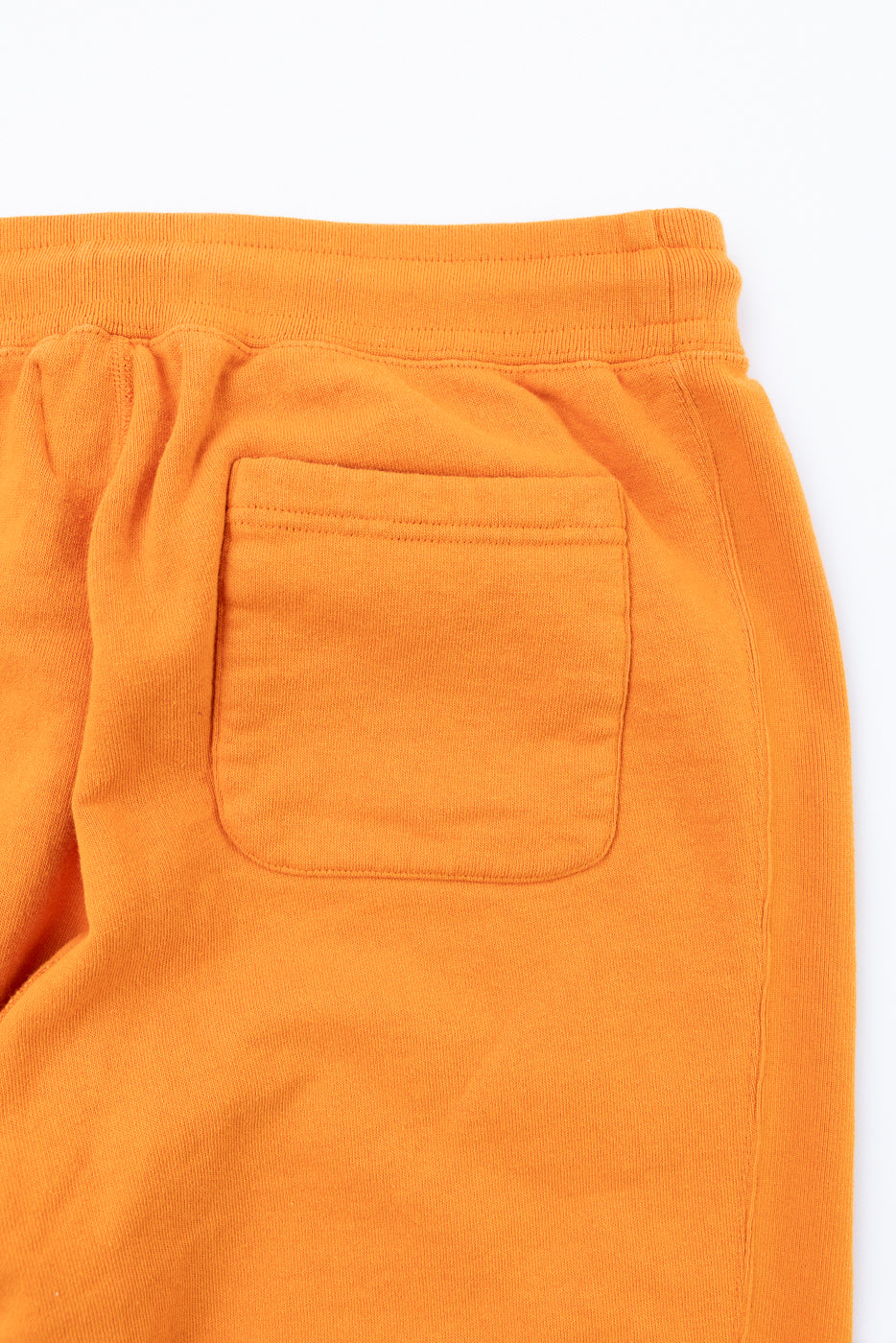 Close-up back view of orange sweatpants showing rear pocket, elastic waistband, and soft fabric texture