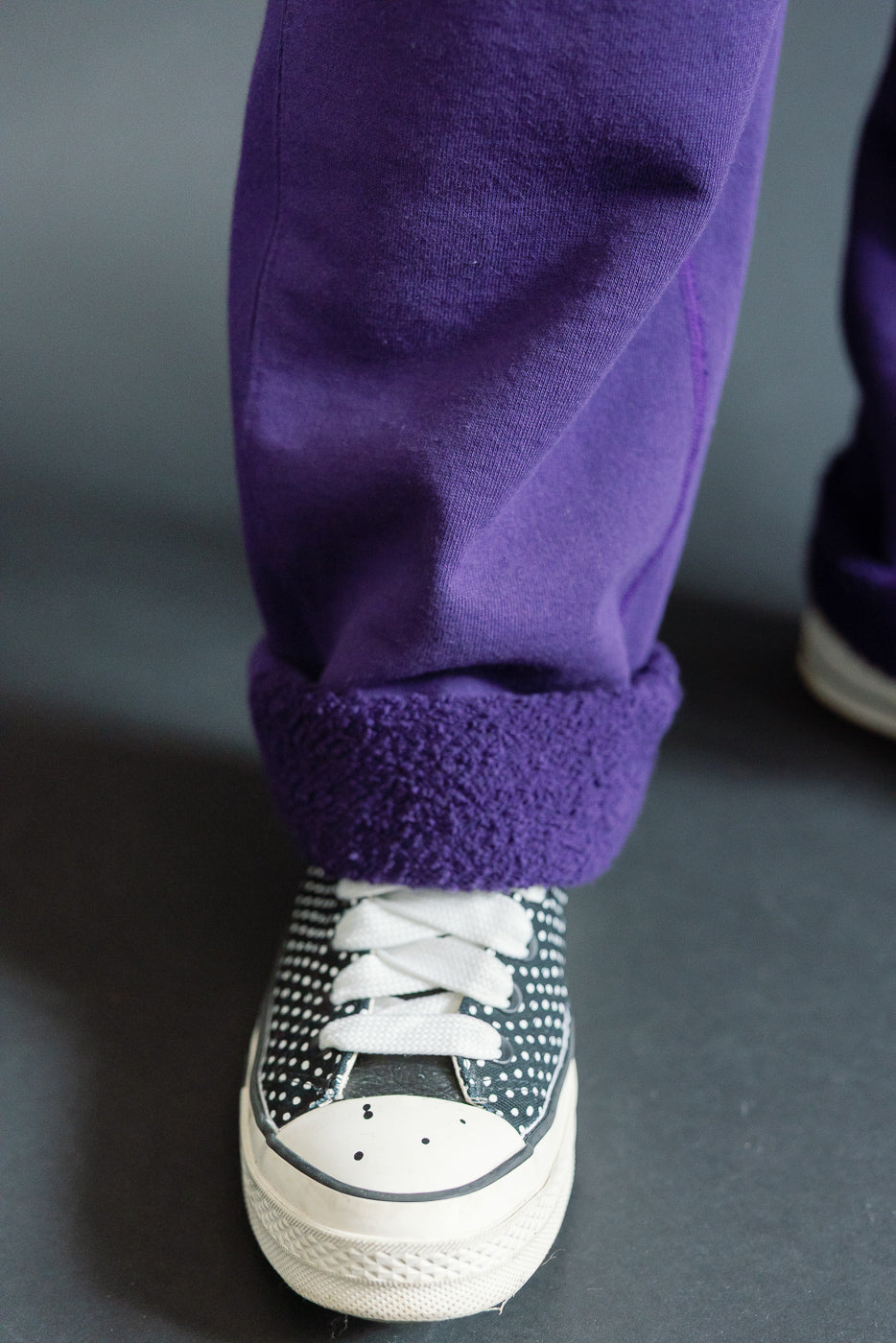 Close-up of male model’s lower leg in purple fleece-lined sweatpants, cuffed hem, paired with polka dot sneakers