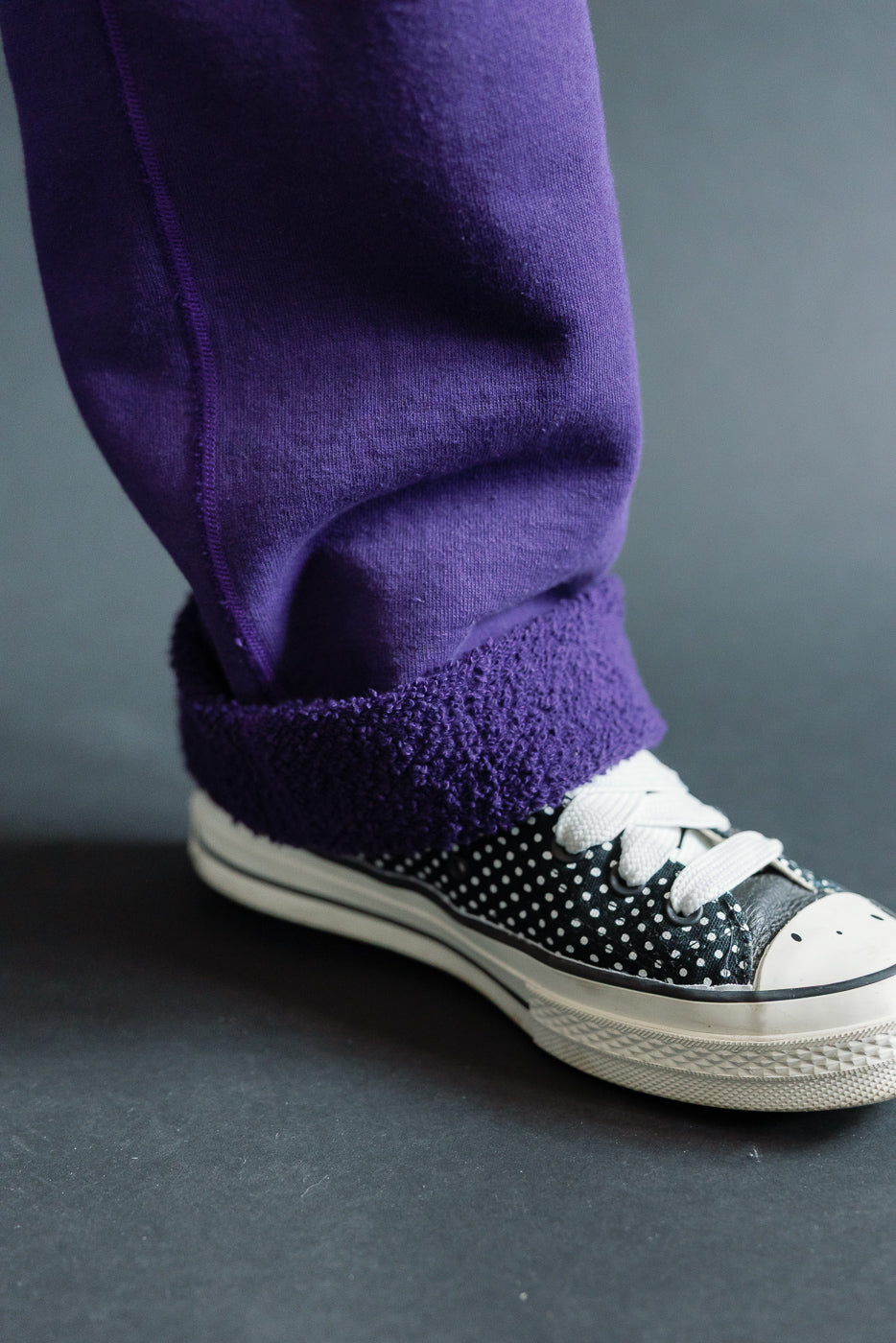Close-up of purple fleece-lined pants hem, worn by male model, paired with polka dot sneakers