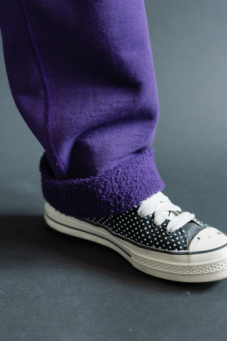 Close-up of purple fleece-lined sweatpants cuff on male model, paired with polka dot sneakers, showing side view