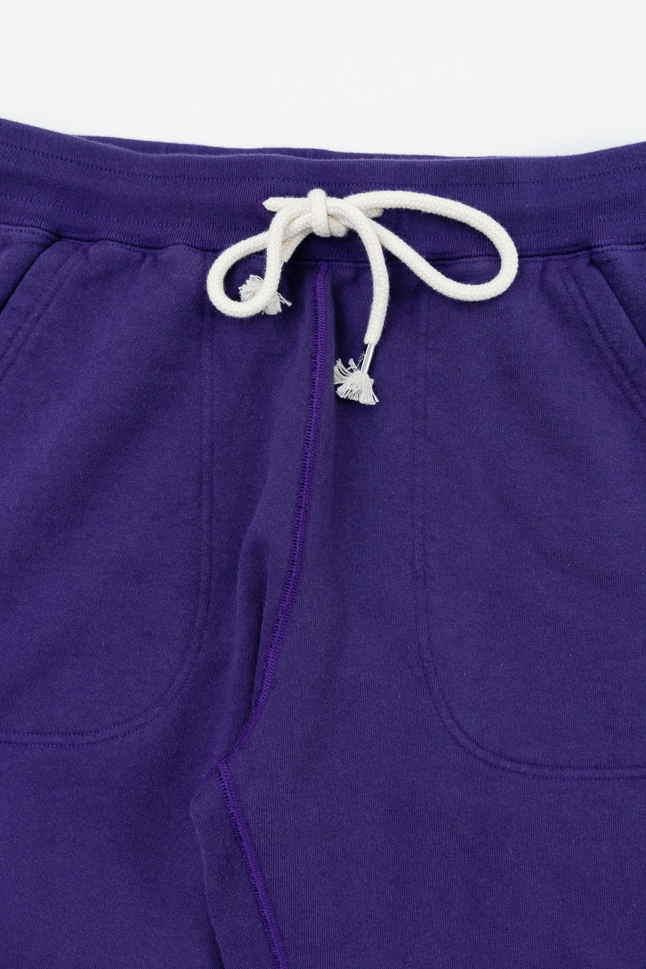 Close-up front of purple joggers with white drawstring, showing texture and side pocket detail