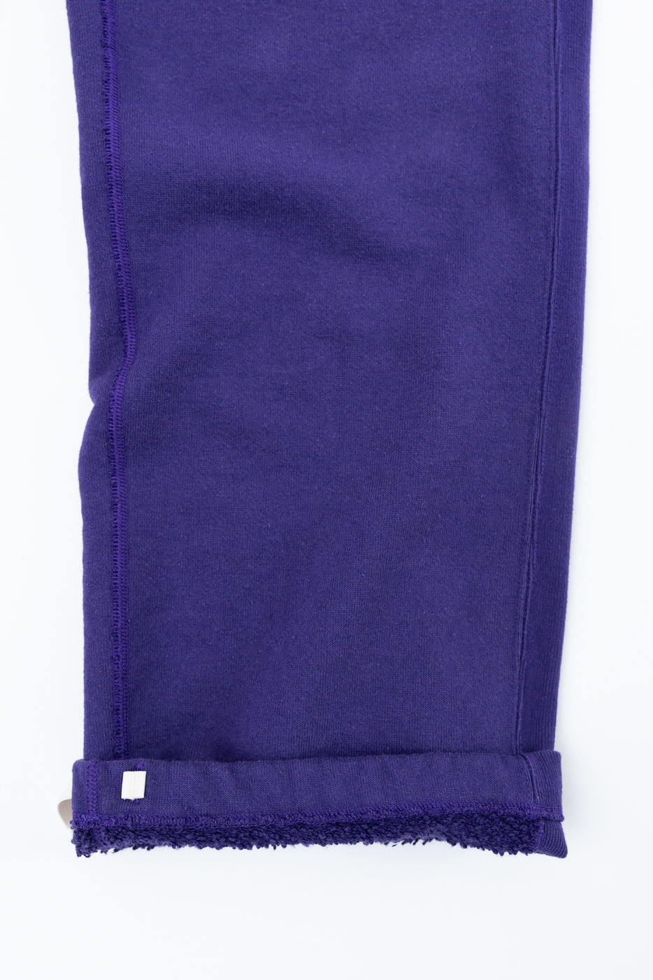 Close-up of purple sweatpants leg, front view, showing cuffed hem with tag and soft fleece lining