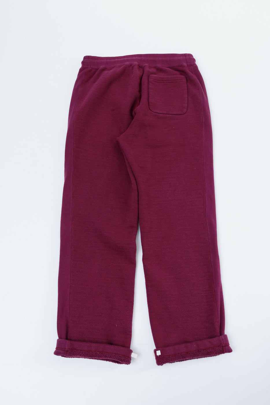 Flat lay showing the back of burgundy sweatpants with a rear pocket and rolled hems.