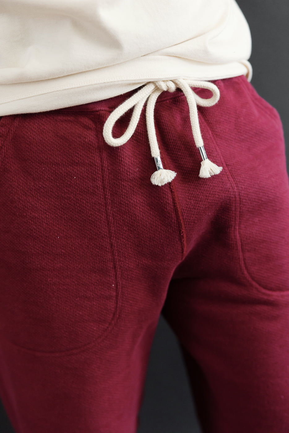 Close-up front view of the waistband and drawstring on burgundy cotton sweatpants.