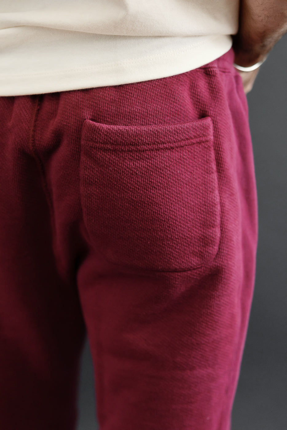 Close-up back view of burgundy sweatpants showing the textured fabric and back pocket.