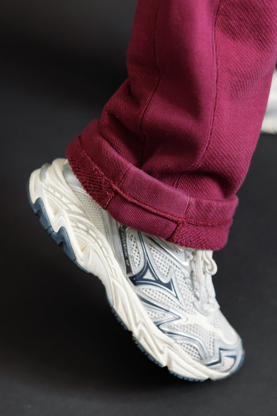Close-up of the bottom hem and cuffed maroon trousers paired with white athletic sneakers.