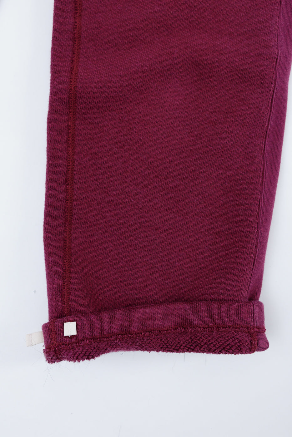 Close-up of the bottom hem and cuff detail of maroon textured fabric trousers, front view.