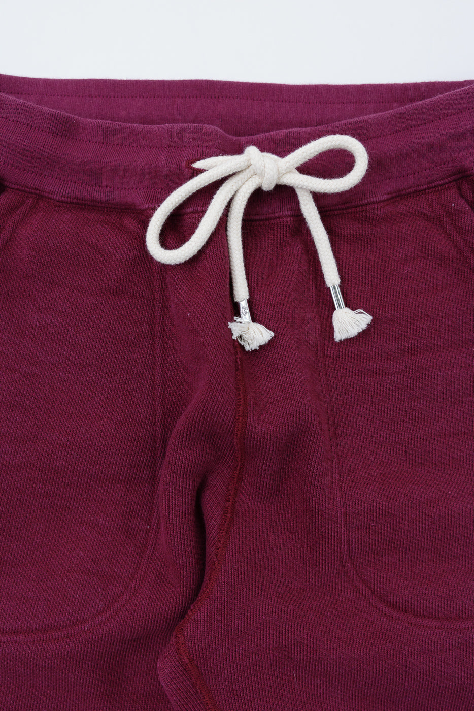 Close-up of the front waistband of burgundy ribbed pants featuring a white drawstring.