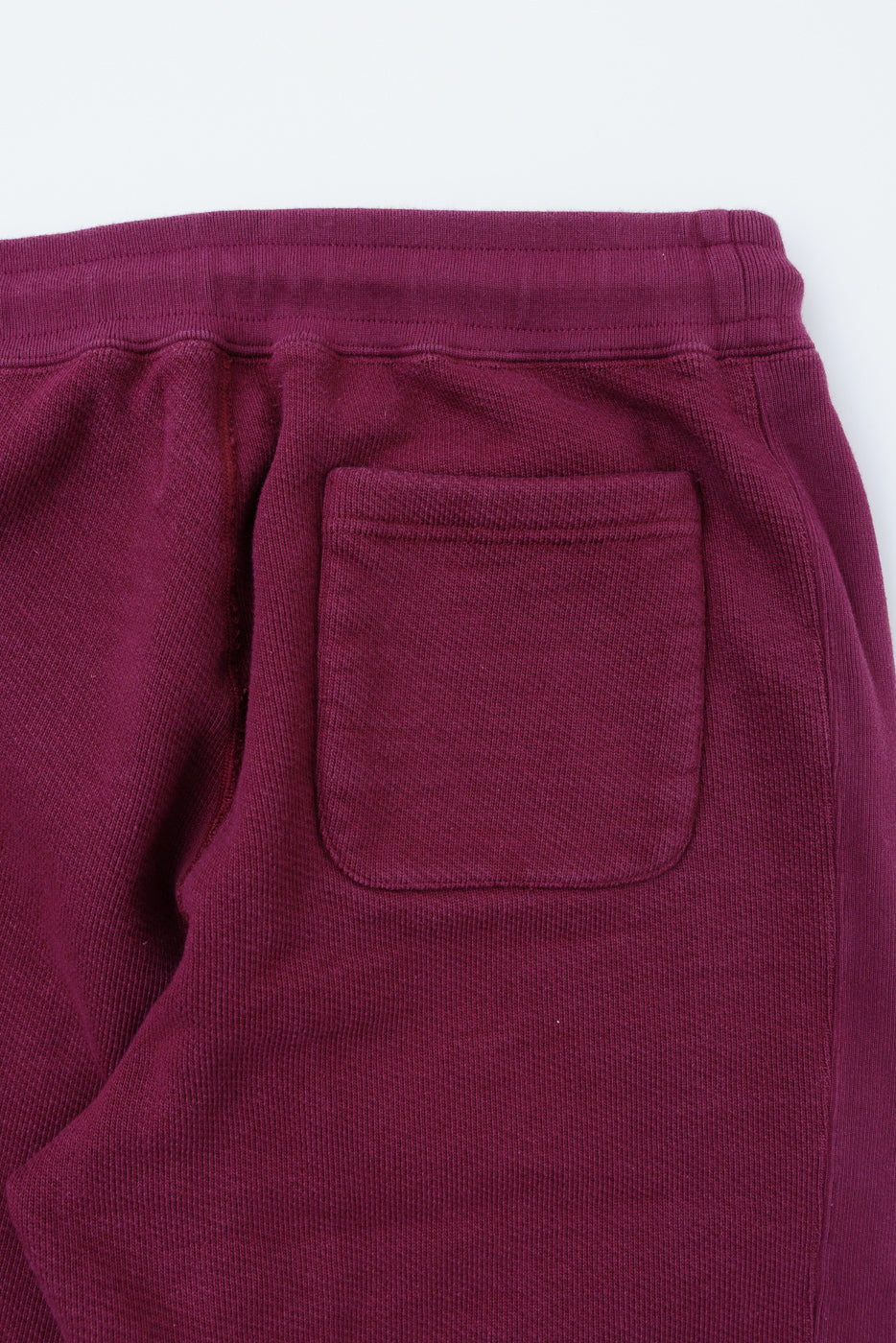 Close-up of the back pocket and ribbed waistband on burgundy cotton sweatpants.