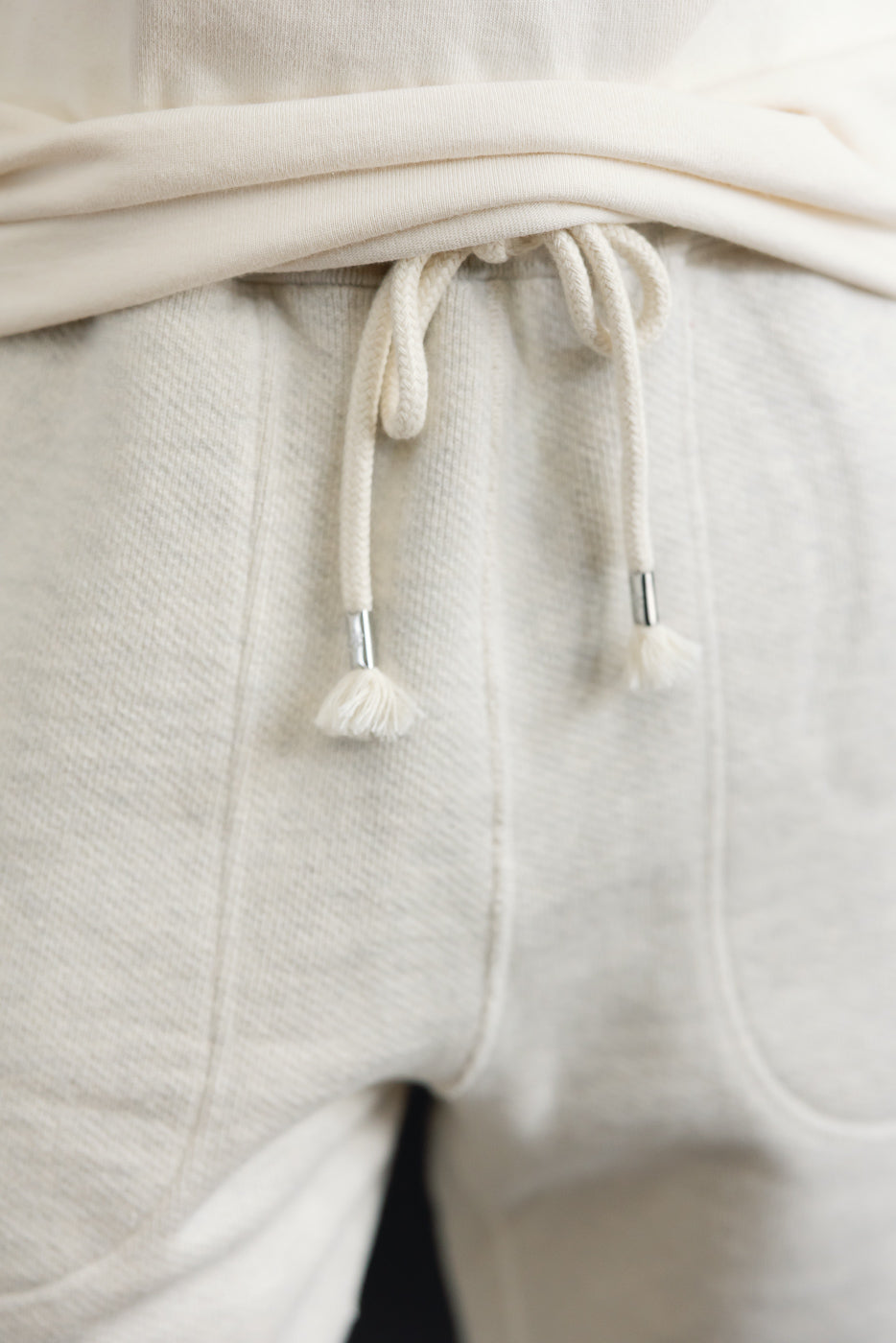 Close-up front view of the waistband and drawstring of cream-colored sweatpants.