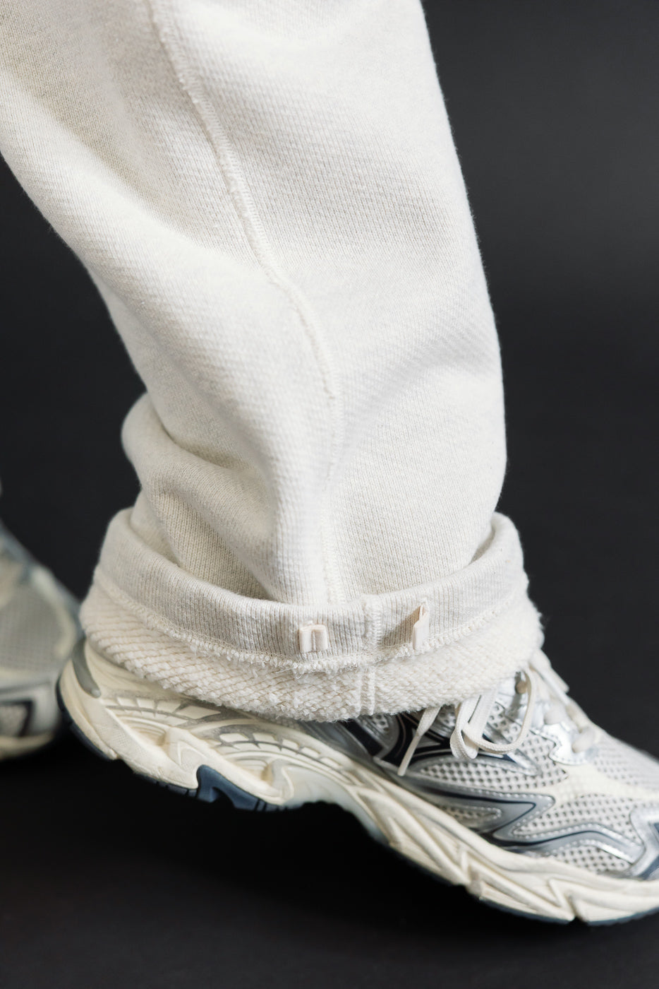 Close-up of the hem of white sweatpants worn by a male model, showing the rolled cuff and fabric texture.