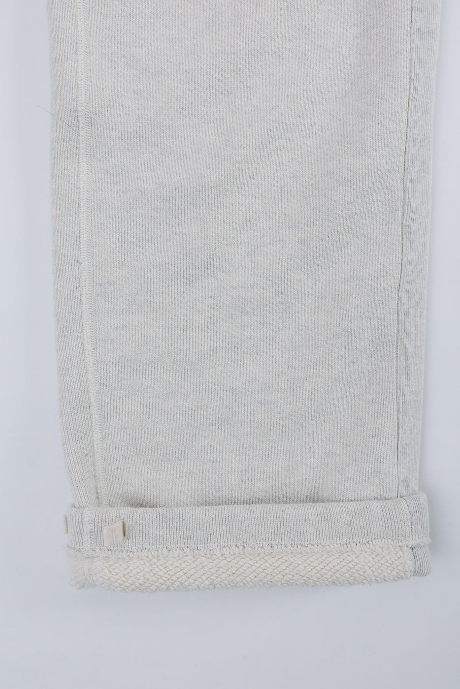 Close-up of the bottom hem and rolled cuff of light grey fleece sweatpants, showing fabric texture.
