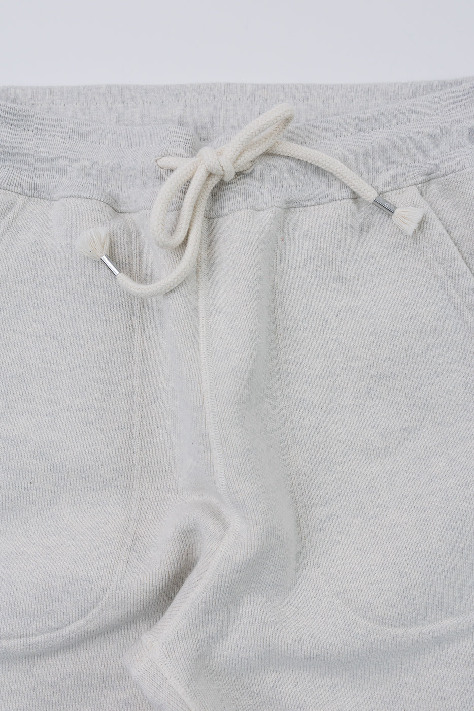 Close-up front view of light grey sweatpants showing the drawstring waistband and fabric texture.