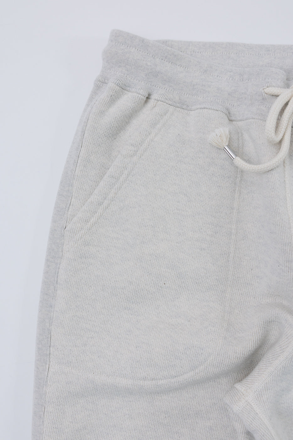Close-up front view of light grey sweatpants showing the elastic waistband and drawstring.
