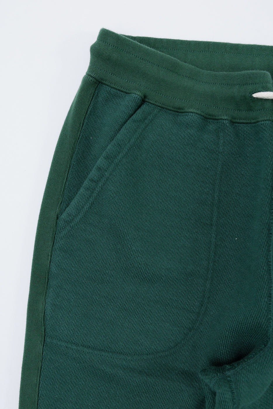 Close-up of the front right side of green ribbed fabric pants showing the waistband and pocket.