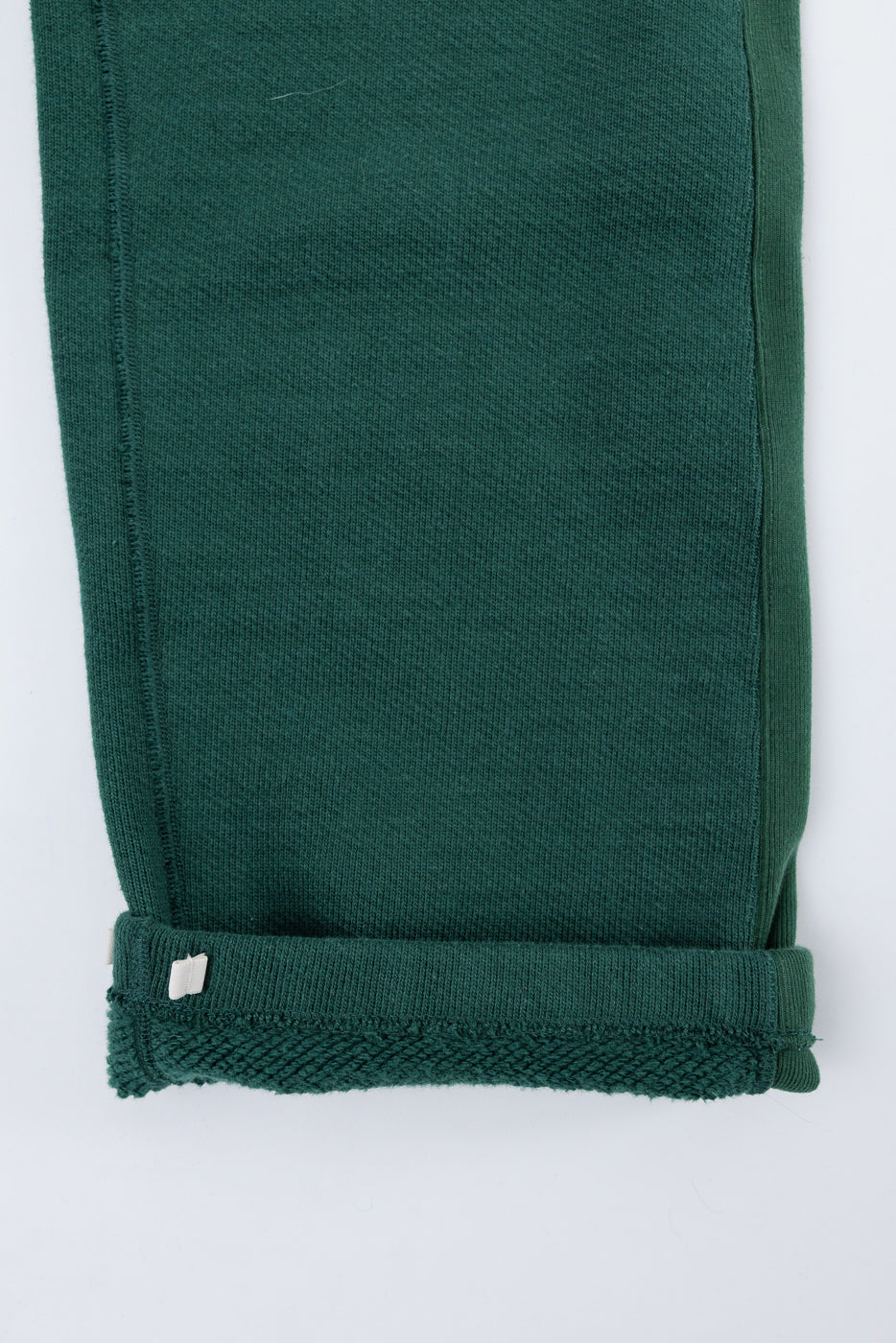 Close-up of the bottom hem and cuff of green textured fabric trousers, side view.