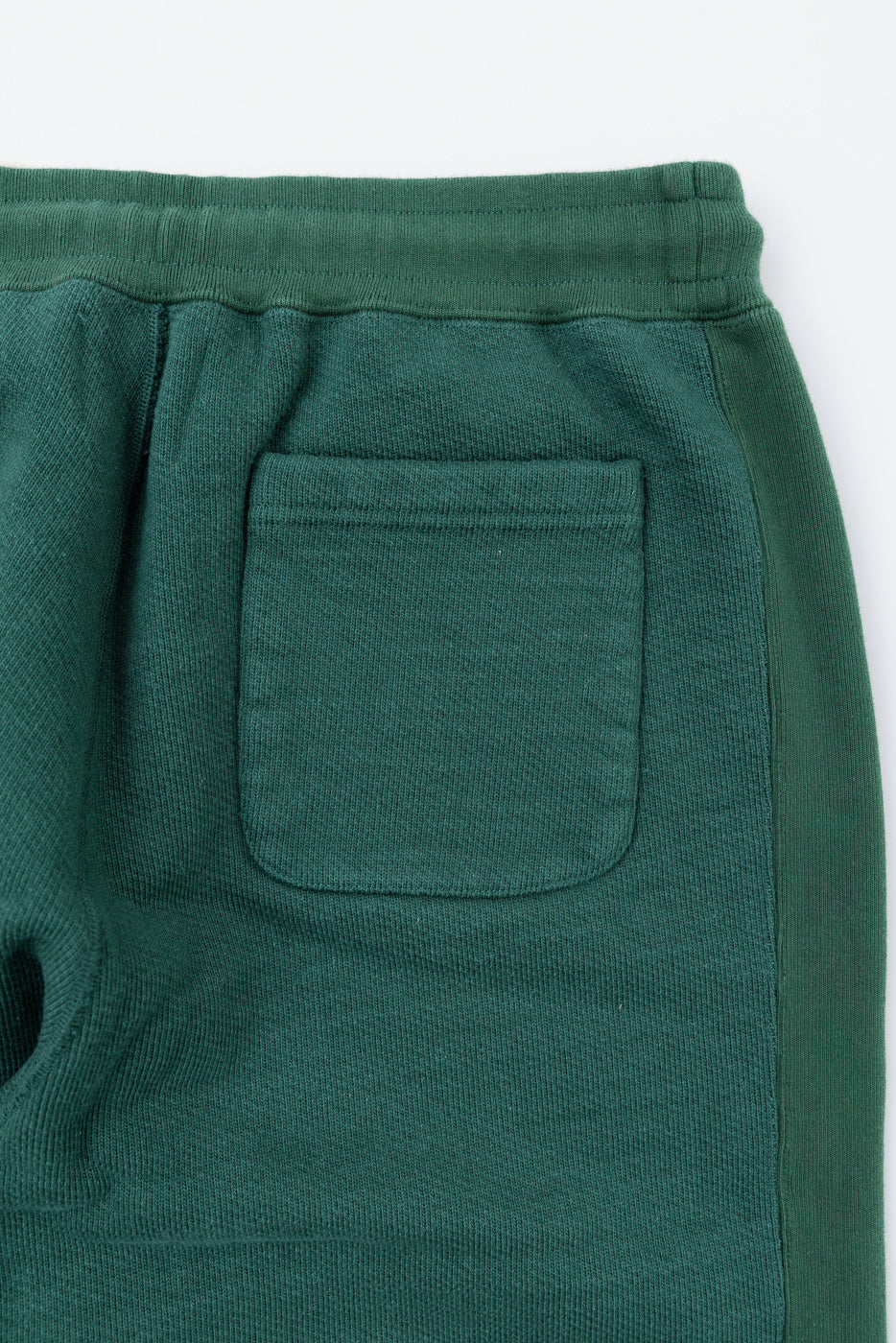 Close-up of the back view of green textured sweatpants showing a patch pocket.