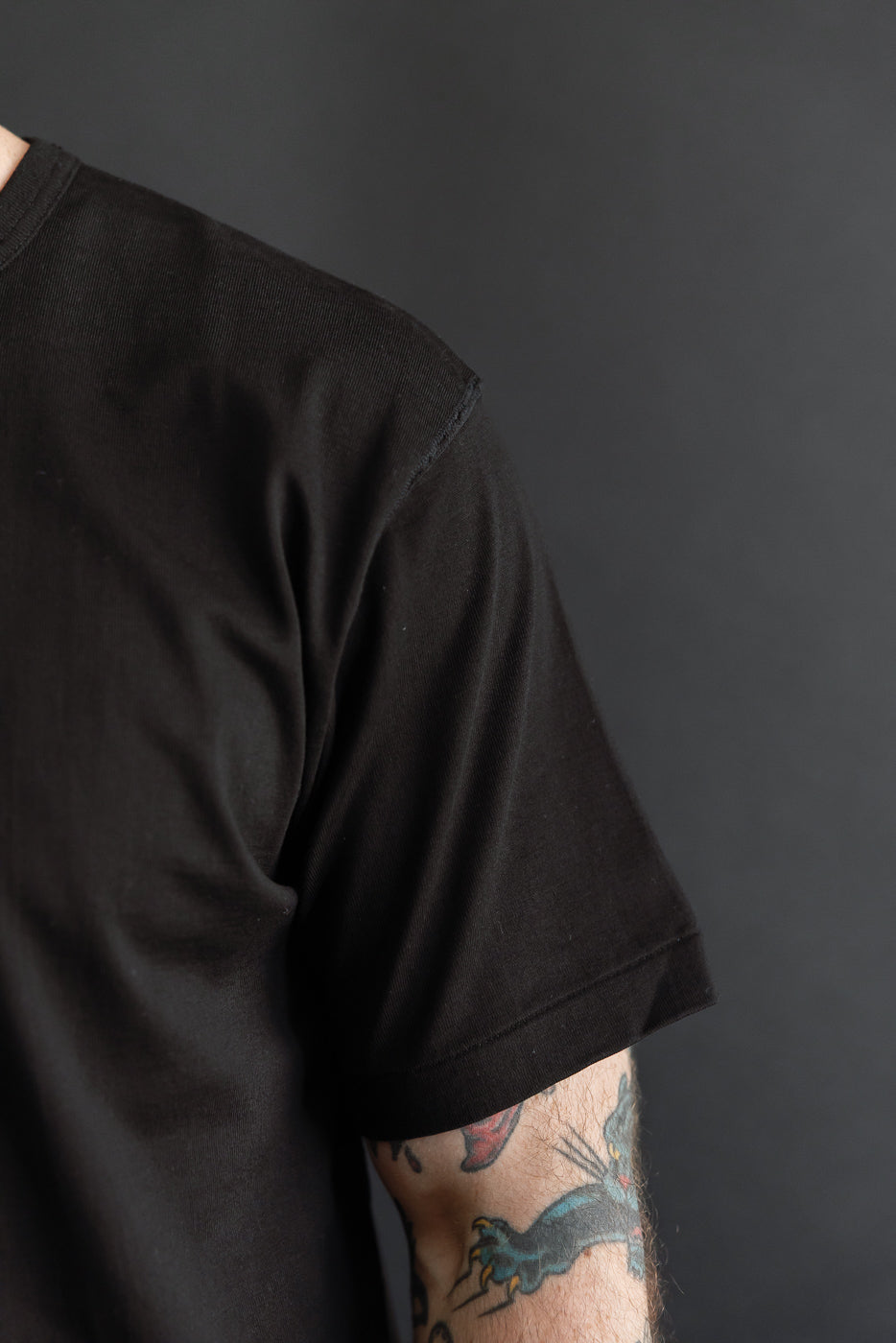 Close-up side view of a male model's black short sleeve t-shirt showing the sleeve and fabric texture.