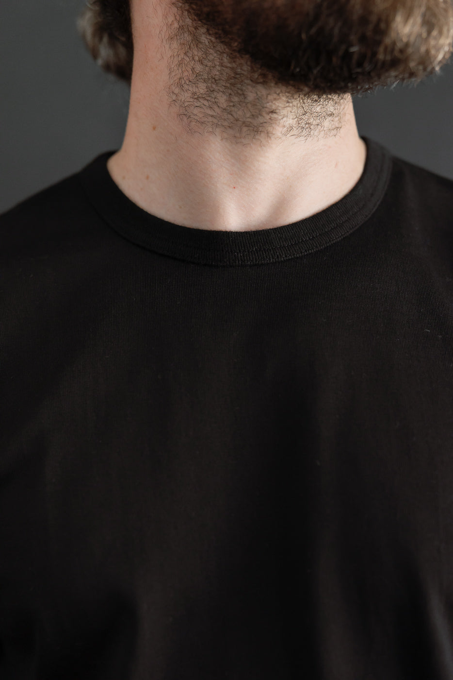 Close-up front view of a black crewneck t-shirt's ribbed collar texture on a male model.