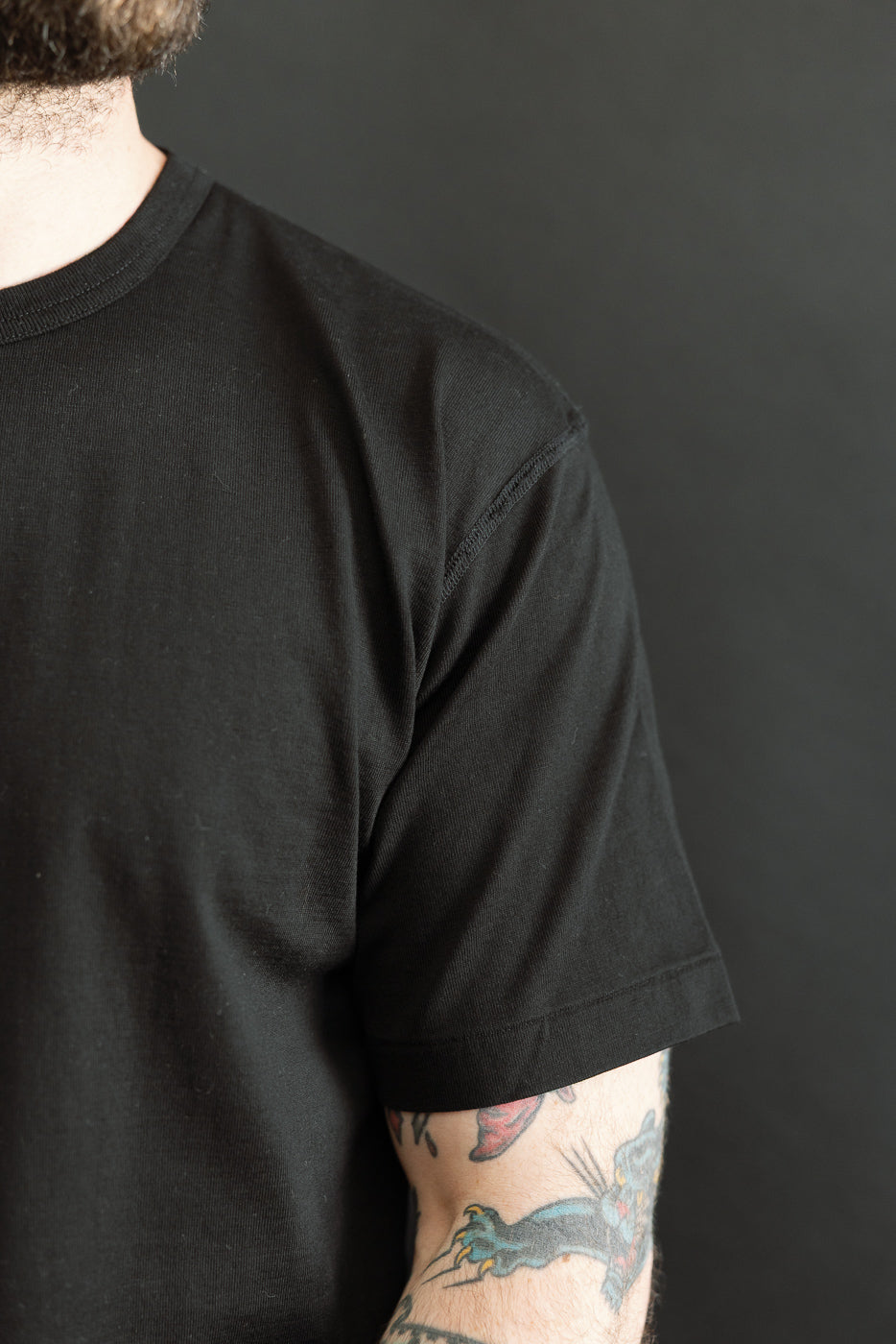 Ultimate Pima Tsuriami Crewneck T-Shirt - Black, showcased on a model's upper torso with a visible colorful panther tattoo on the forearm, highlighting the shirt's smooth texture and premium Japanese craftsmanship.