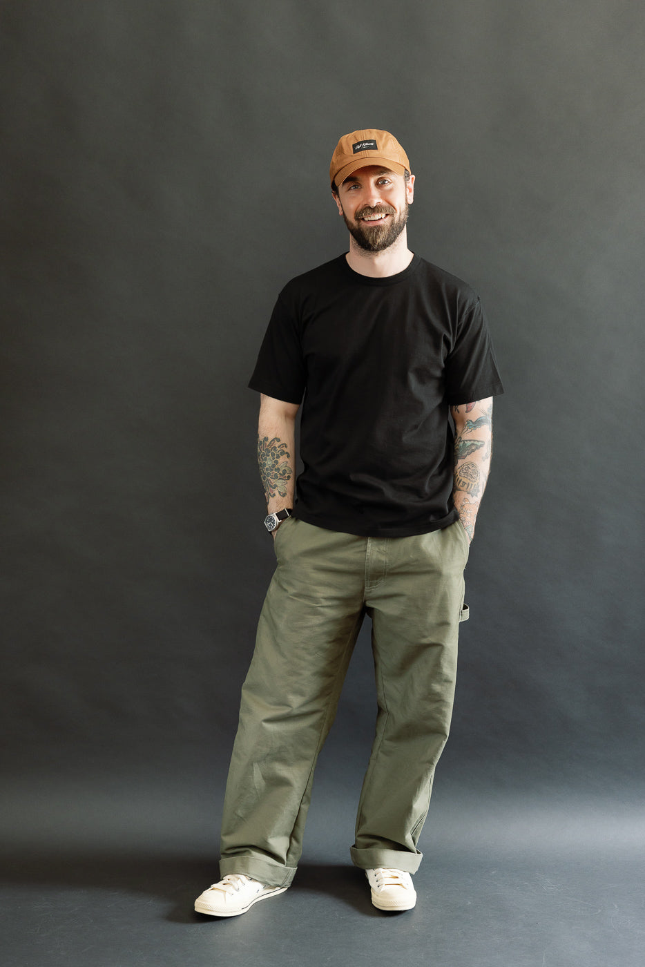 Man wearing the Ultimate Pima Tsuriami Crewneck T-Shirt - Black, styled with olive-green pants and off-white sneakers, showcasing the shirt's lightweight, smooth texture, and athletic fit against a dark-gray backdrop.
